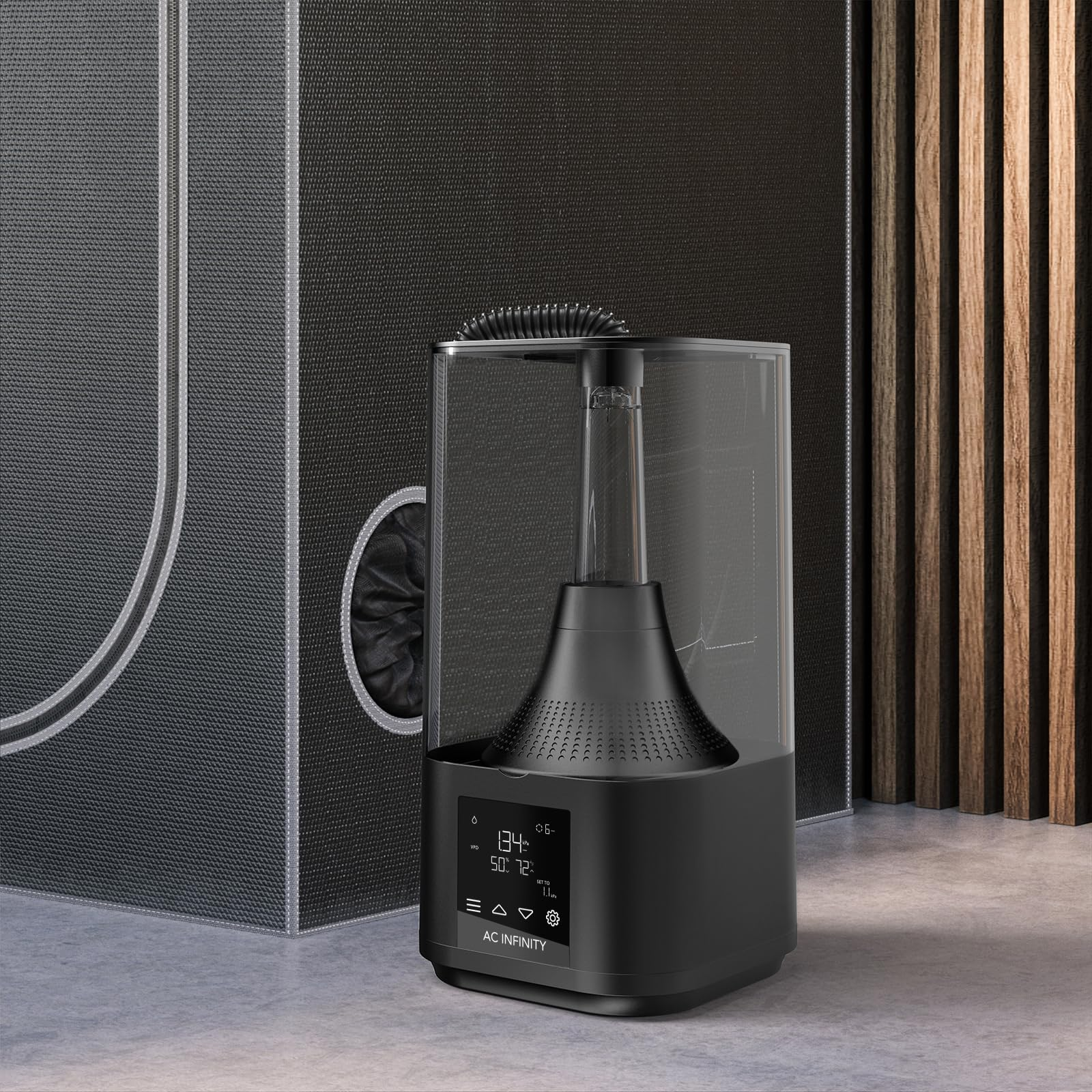 Un humidificateur noir AC Infinity sur un sol gris devant une tente sombre et des lattes en bois.