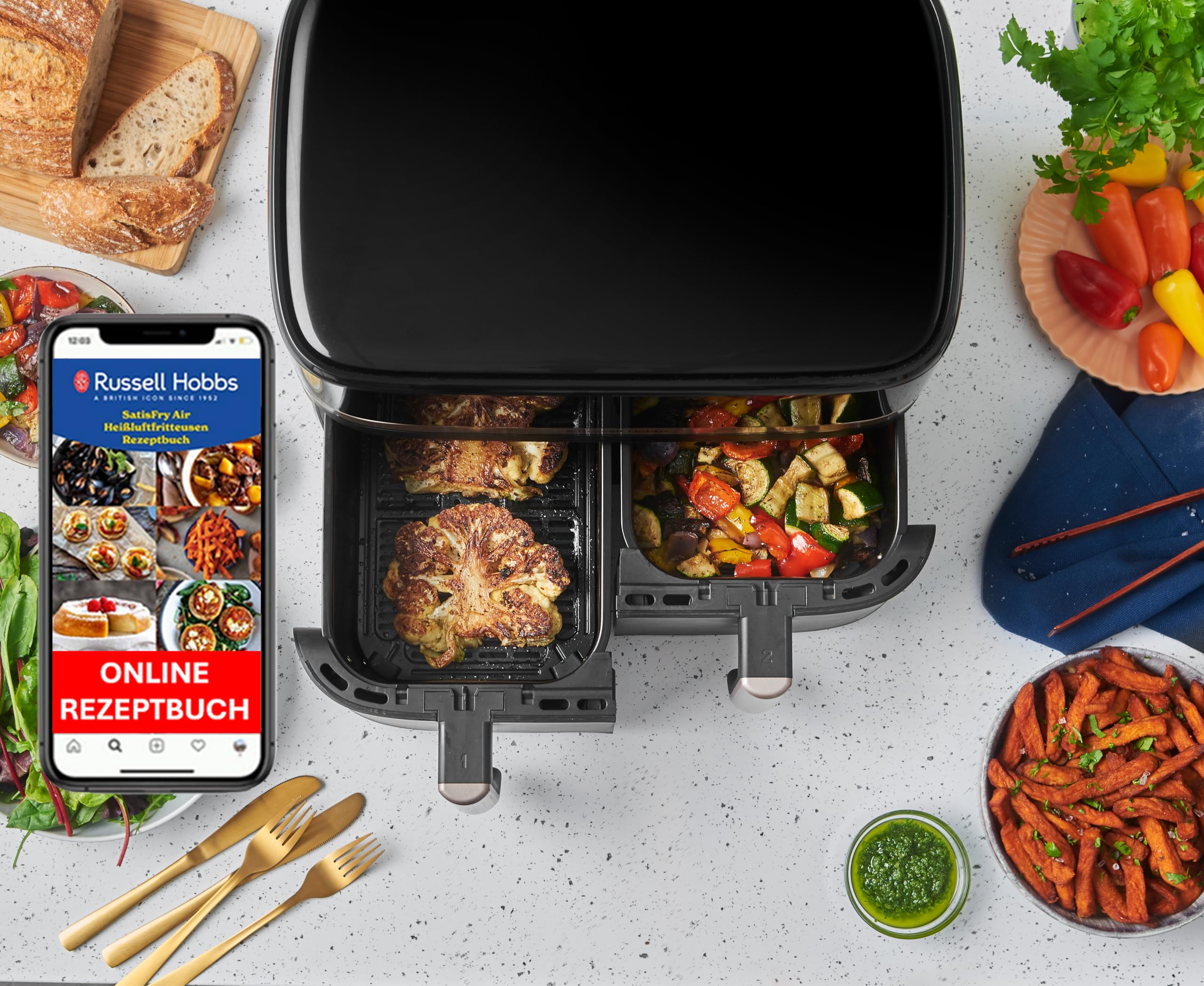 Friteuse sans huile à double panier avec chou-fleur et légumes cuits, à côté d'un smartphone affichant des recettes.