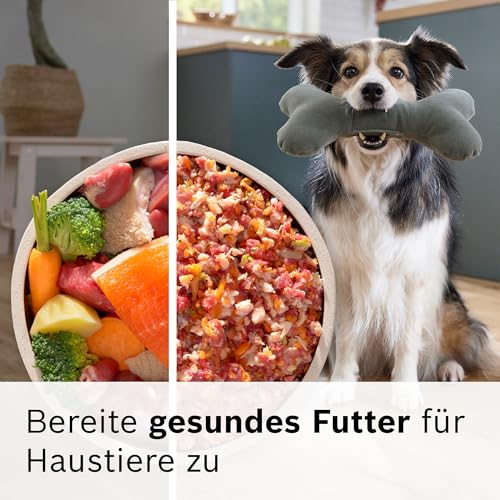 Ein Hund hält einen Stoffknochen im Maul neben einer Schüssel mit frischen rohen Zutaten und gesundem Futter.
