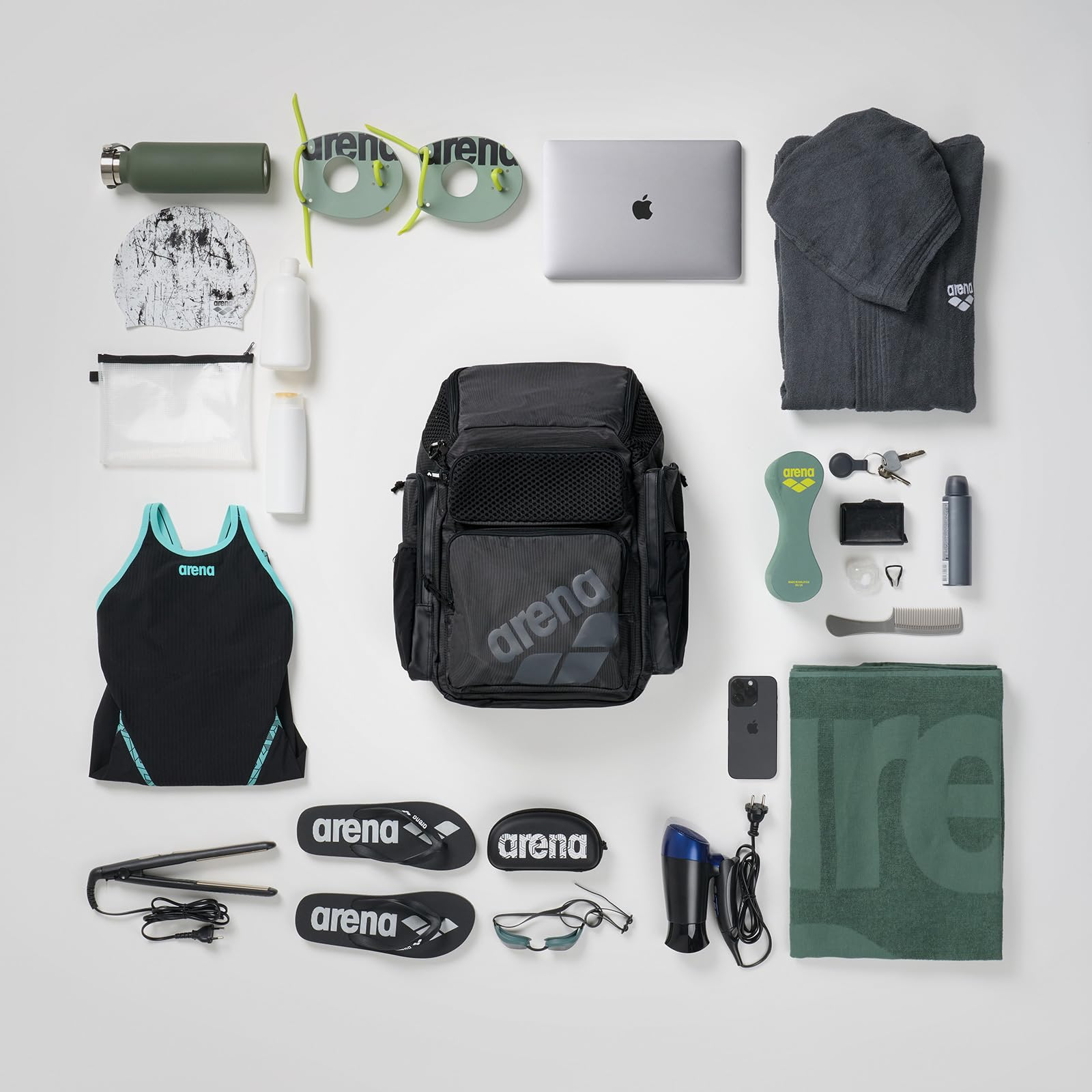 Ein Rucksack umgeben von Schwimmausrüstung, Laptop, Handtuch und persönlichen Gegenständen auf grauem Hintergrund.