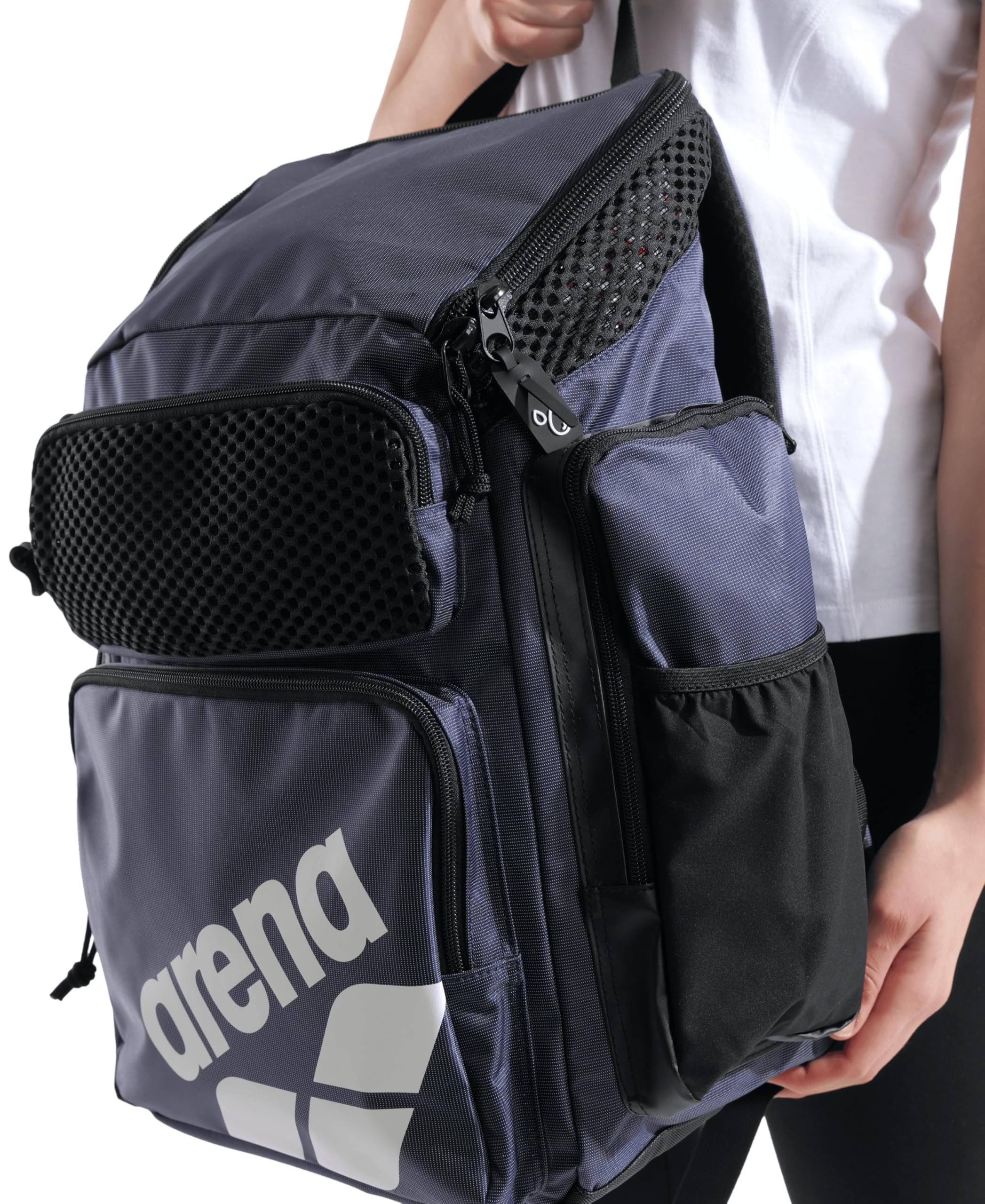 Eine Person trägt einen dunkelblauen Arena Rucksack mit mehreren Taschen und weißem Logo.