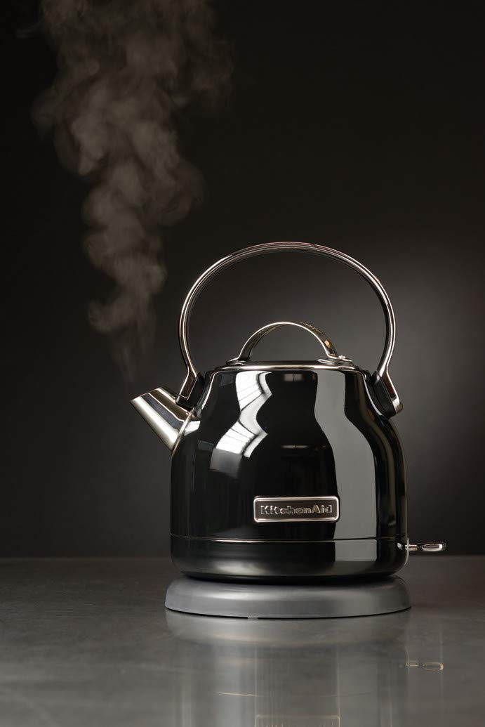 Ein schwarzer KitchenAid-Wasserkocher auf einem Sockel mit aufsteigendem Dampf vor dunklem Hintergrund.