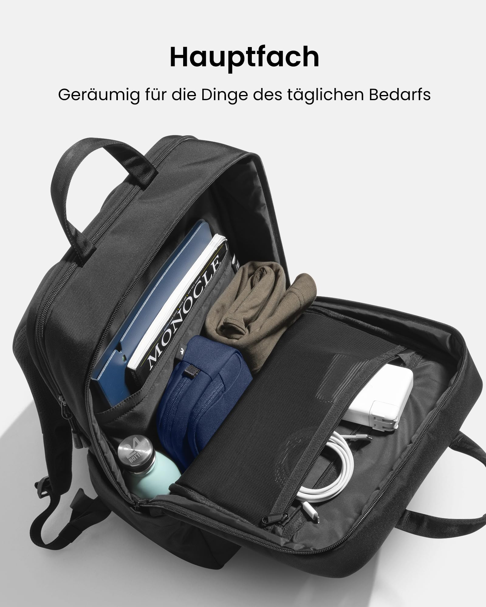 Ein offener schwarzer Rucksack gefüllt mit Laptop, Magazin, Kleidung, blauem Etui, Trinkflasche und Ladekabeln.