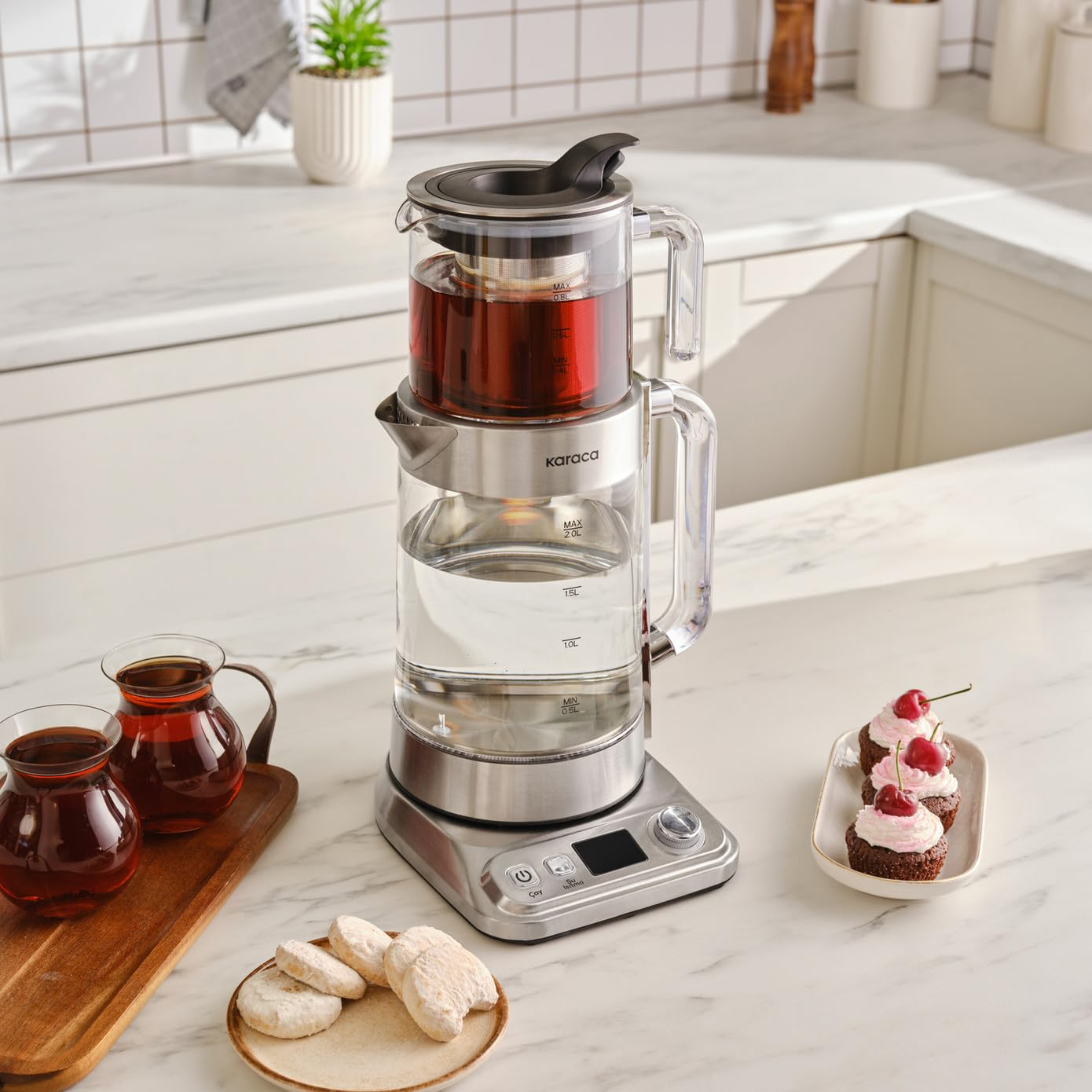 Mutfak tezgahında cupcake ve kurabiyelerle birlikte duran modern çift camlı çaycı.