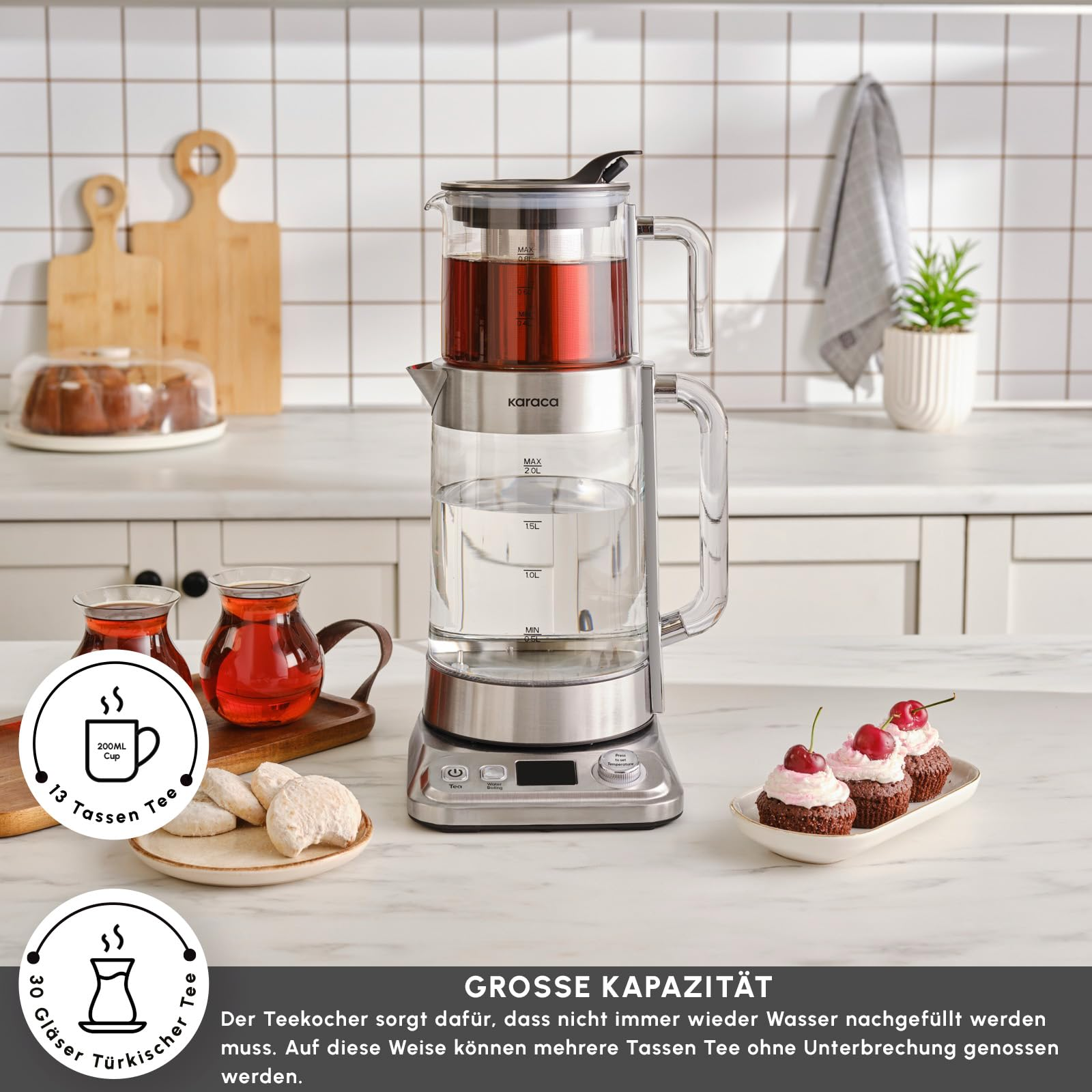 Mutfak tezgahında çay bardakları, kurabiyeler ve keklerle birlikte çift katlı cam çay makinesi.