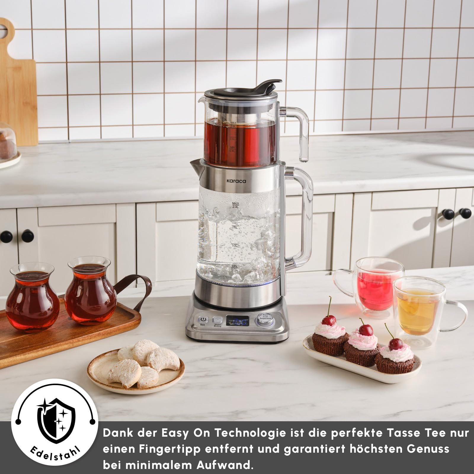 Mermer tezgah üzerinde çay bardakları, cupcake ve kurabiyelerle çevrili ikili cam çay makinesi.