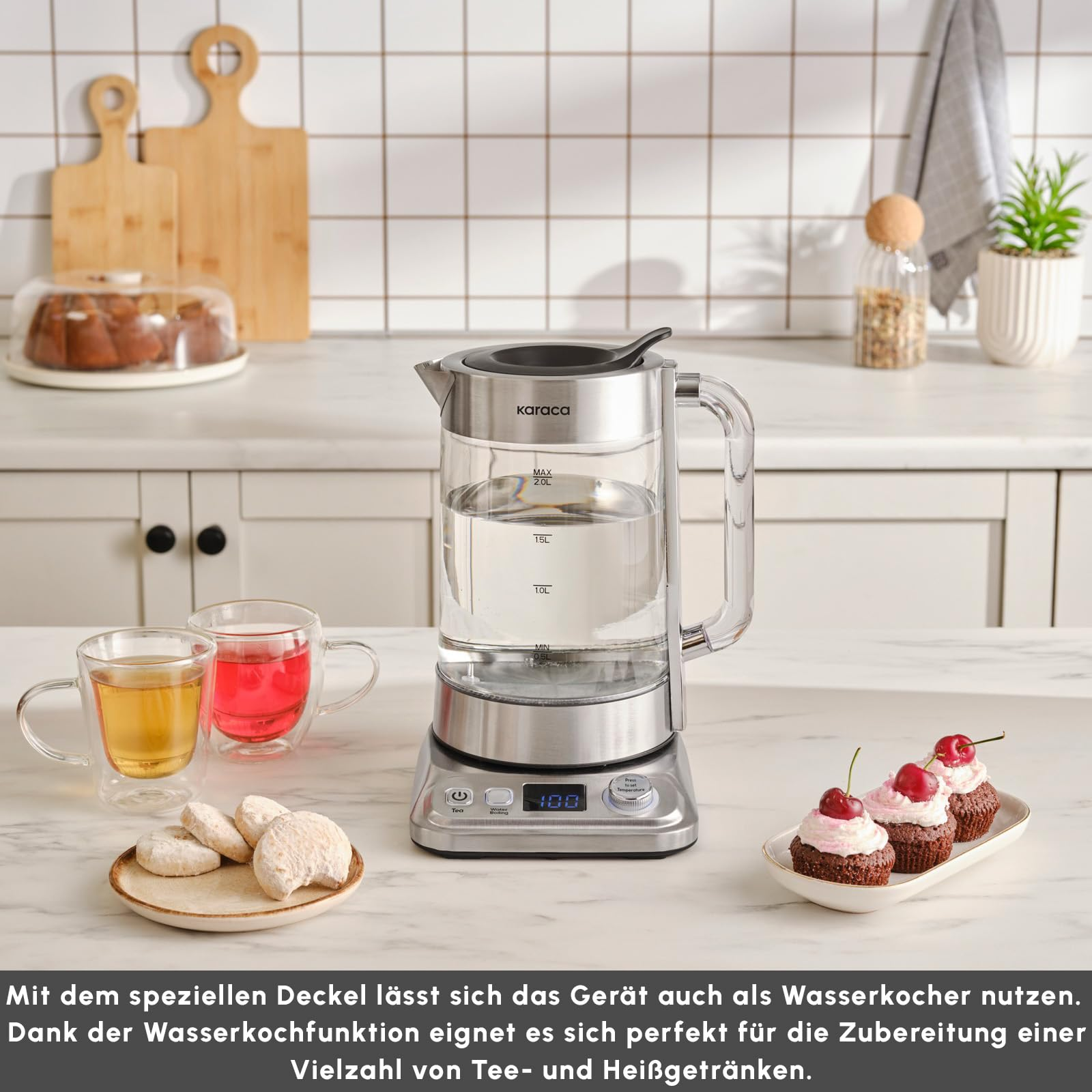 İki bardak çay, kurabiye ve cupcake ile mutfak tezgahında duran cam su ısıtıcısı.