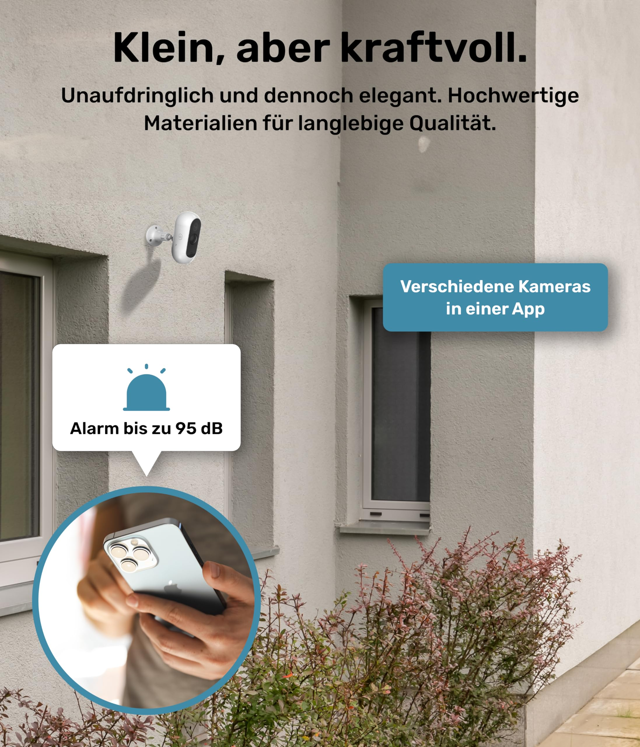 Una telecamera di sicurezza su un muro bianco, con schermo del telefono e testo.