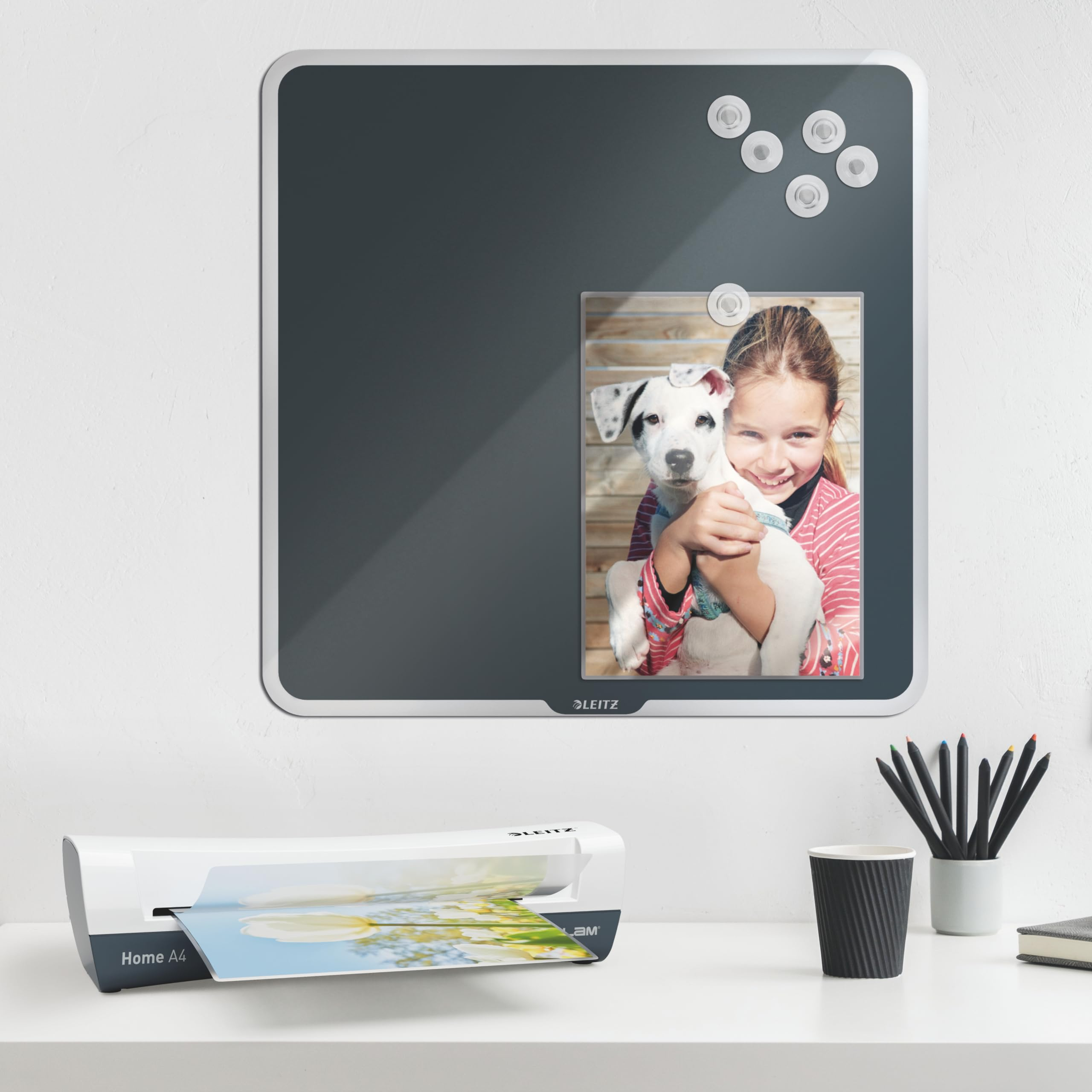 Un tableau magnétique avec photo, plastifieuse, pot à crayons et gobelet en papier sur un bureau blanc.