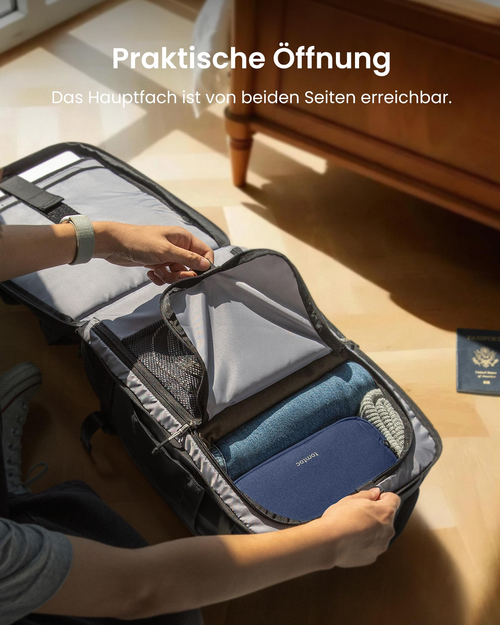 Person öffnet einen schwarzen Rucksack auf dem Boden, gefüllt mit Kleidung und einem blauen Etui.
