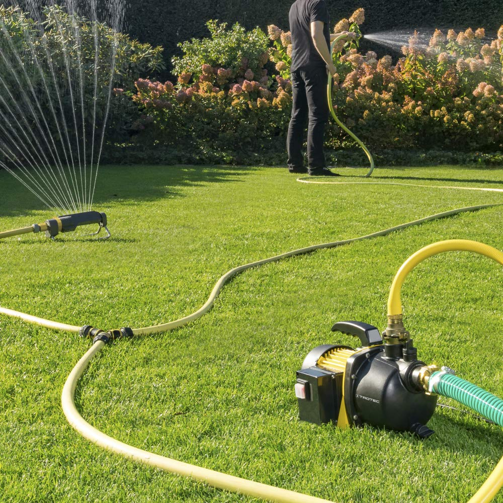 Eine Wasserpumpe und ein Rasensprenger bewässern einen grünen Garten, während eine Person mit einem Schlauch hantiert.