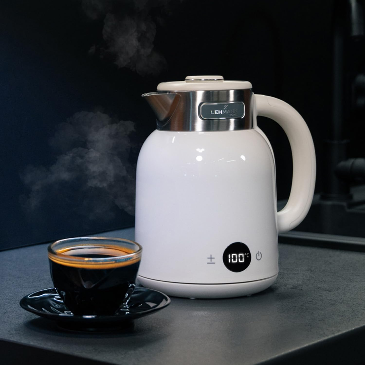 Un bollitore elettrico bianco con display digitale e una tazza di caffè fumante si trovano su un piano scuro.