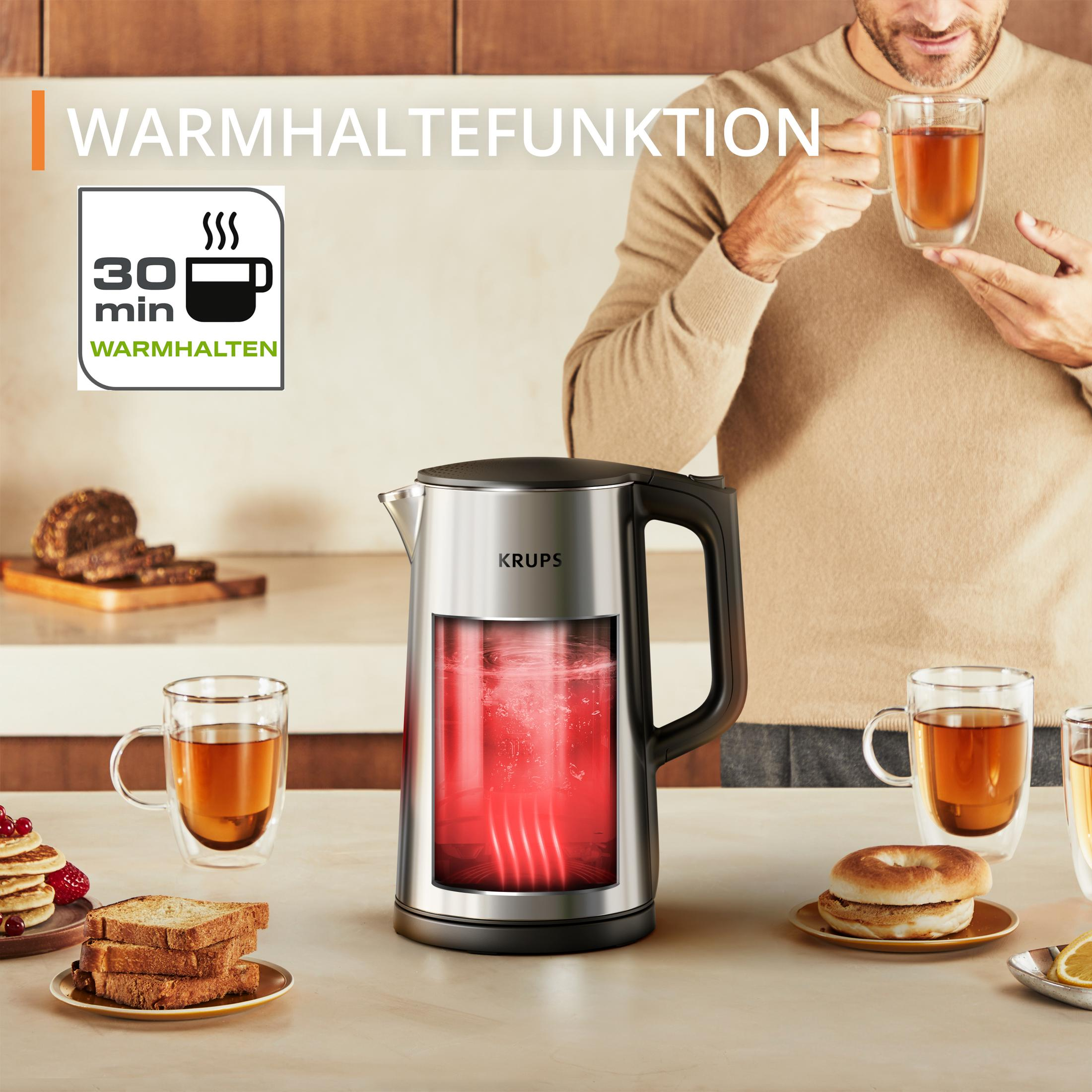 Bollitore Krups con elemento luminoso rosso su un piano cucina, circondato da tazze di tè e pane.