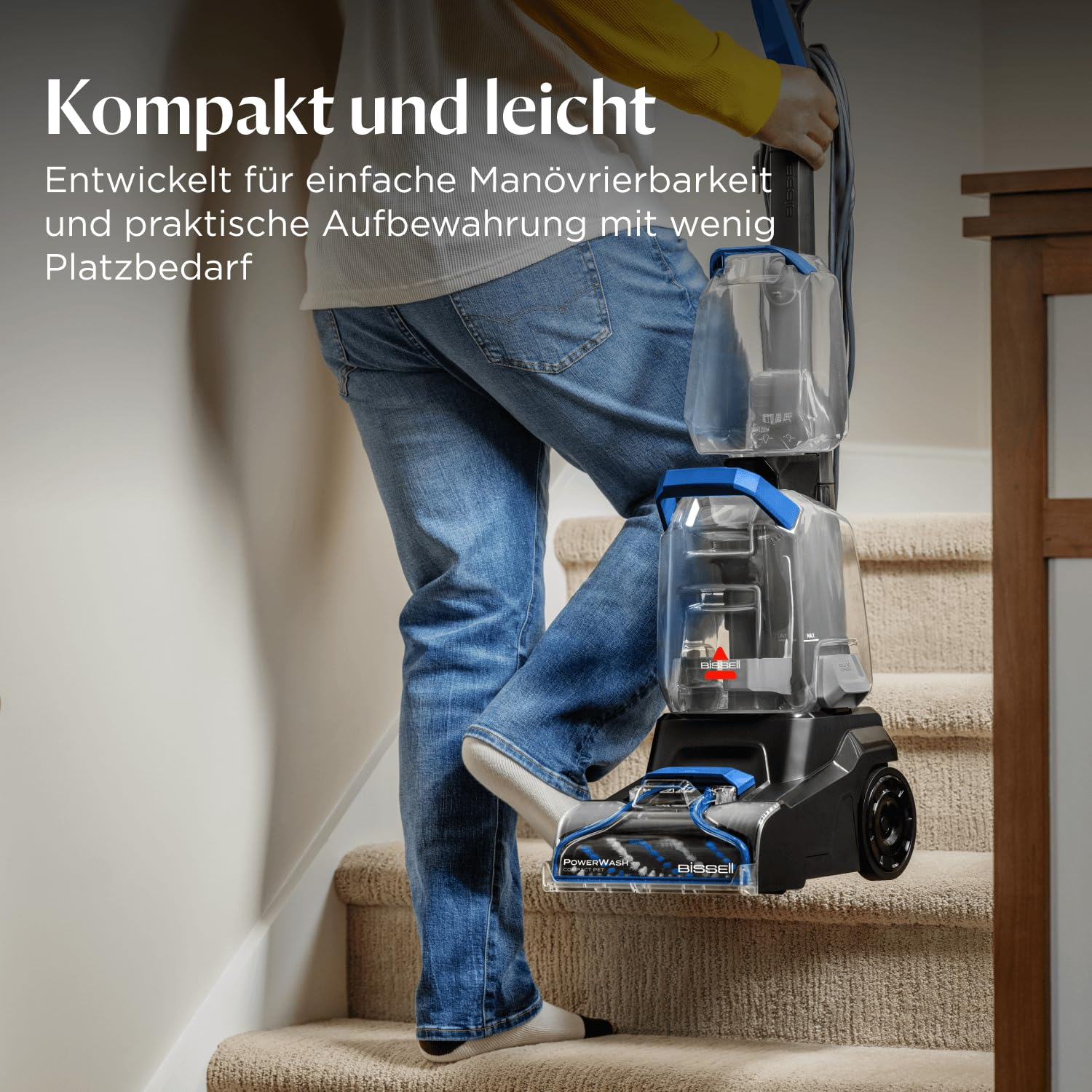 Una persona con jeans e calzini bianchi porta un pulitore Bissell compatto su scale con moquette.