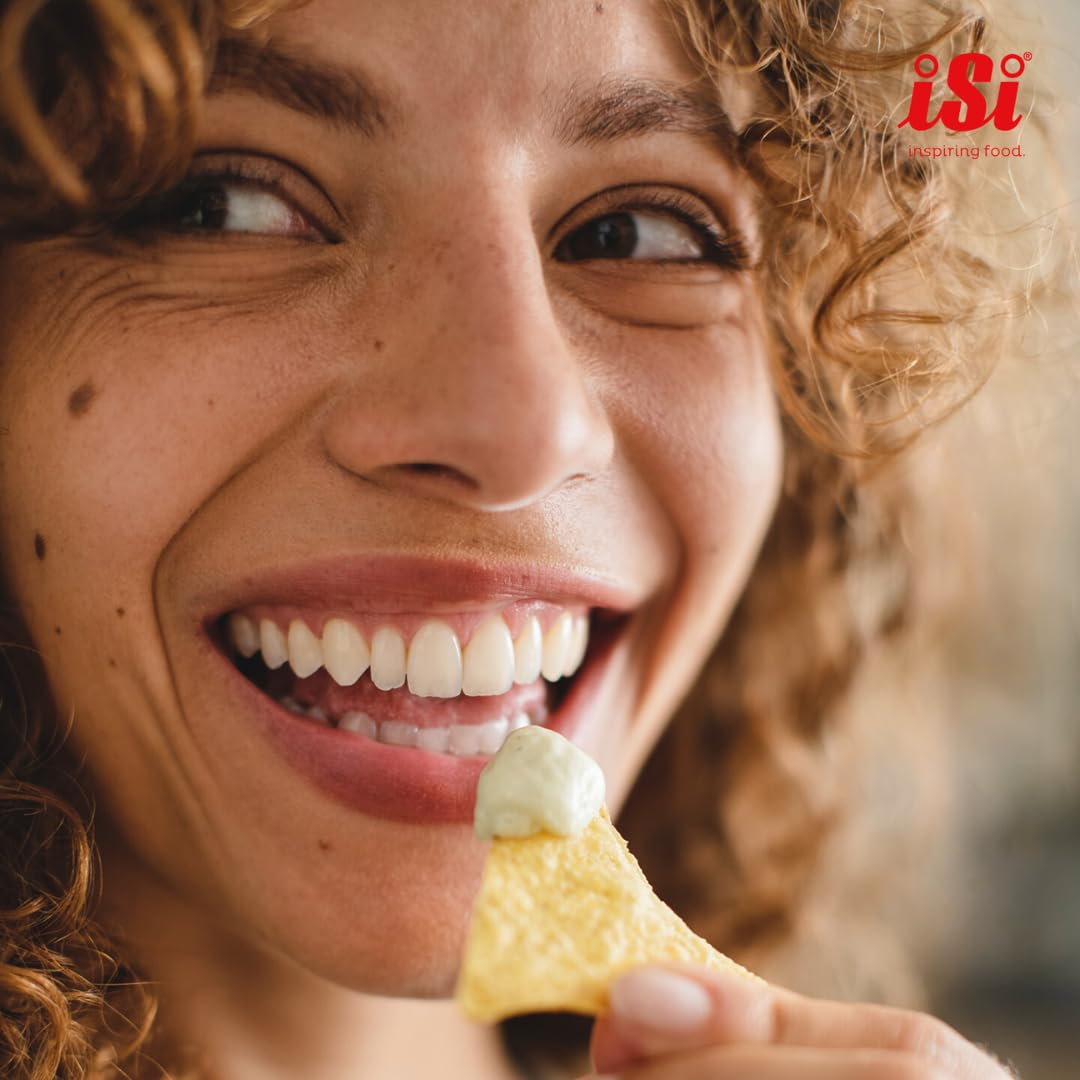 Une femme souriante aux cheveux bouclés tient une tortilla avec de la sauce près de sa bouche.