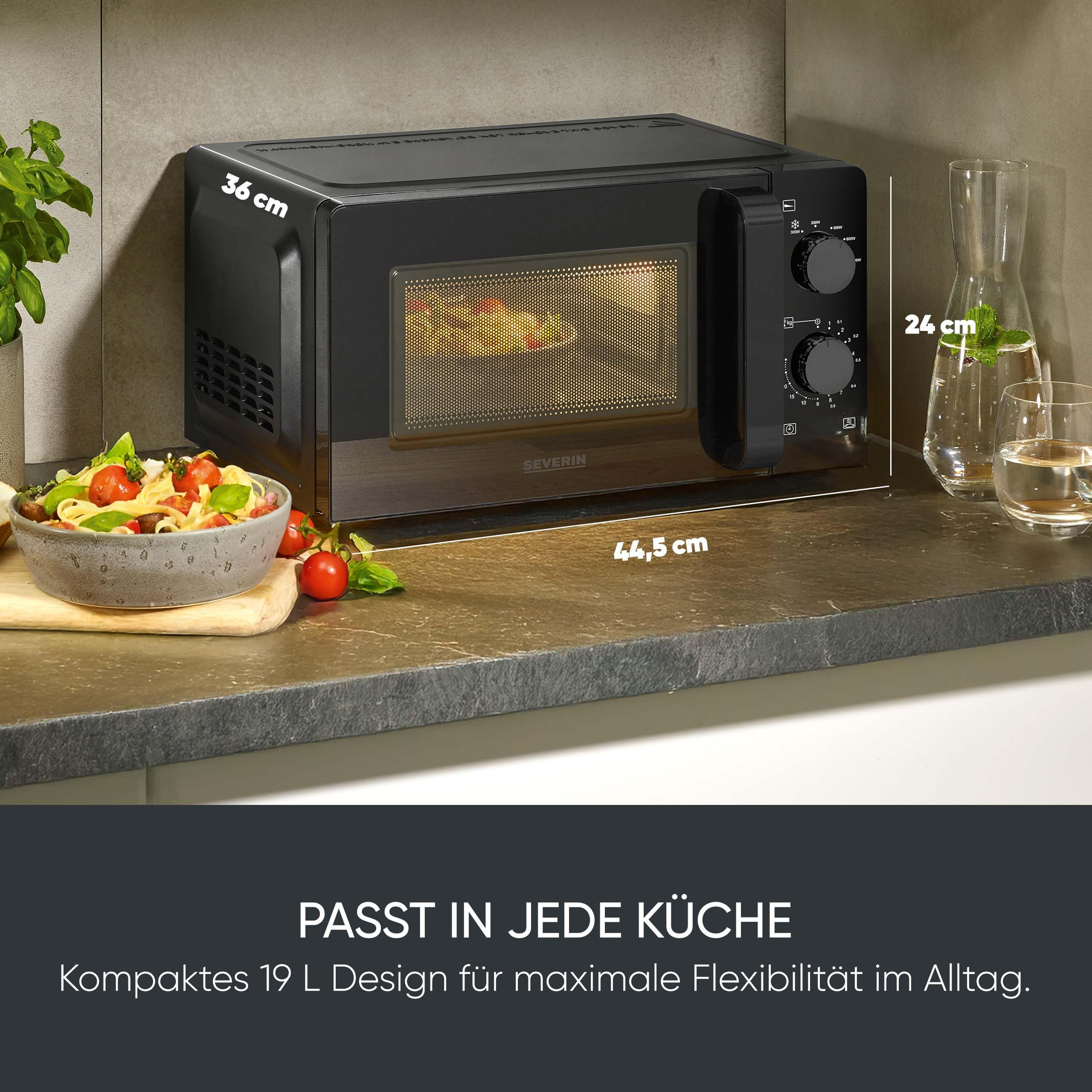 Schwarze Severin Mikrowelle mit Maßen auf einer Küchenarbeitsplatte, daneben Salat und Wasser.