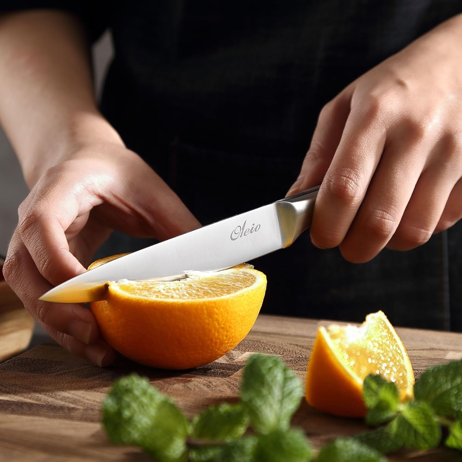 Eine Person schneidet eine halbe Orange mit einem silbernen Messer auf einem Holzbrett mit Minze.