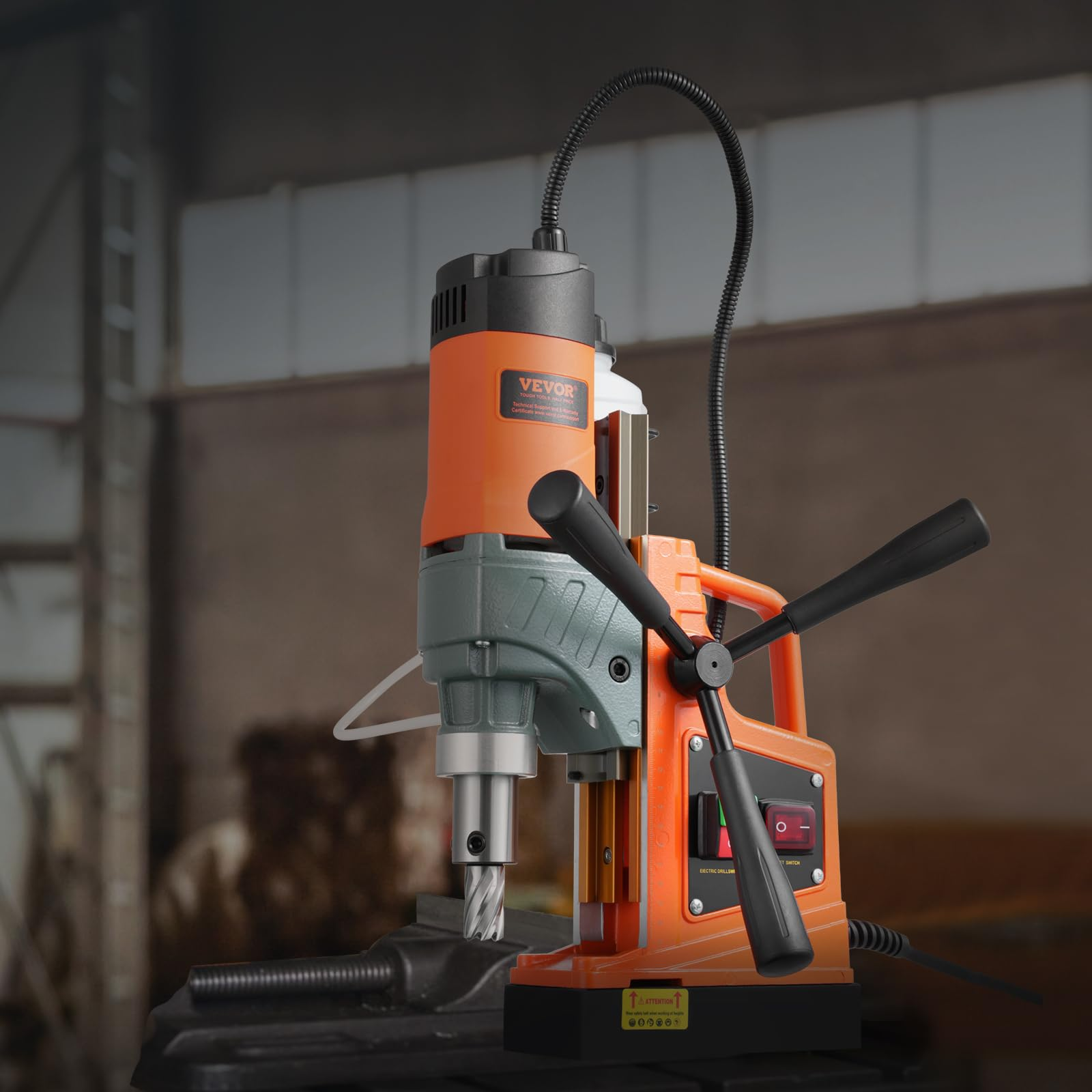 Eine orange-schwarze Magnetbohrmaschine steht in einer Werkstatt auf einem Tisch.