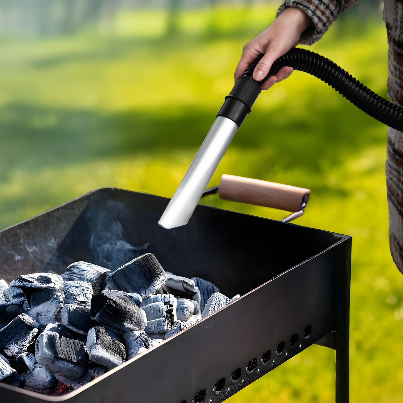 Persona che tiene il tubo dell'aspirapolvere sopra il grill con carbone fumante all'aperto.