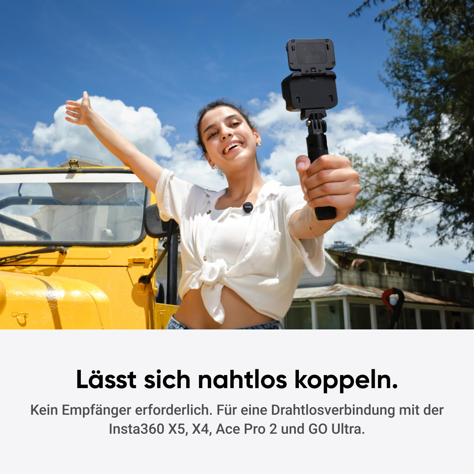 Eine lächelnde Frau hält eine Kamera vor einem gelben Auto und blauem Himmel.