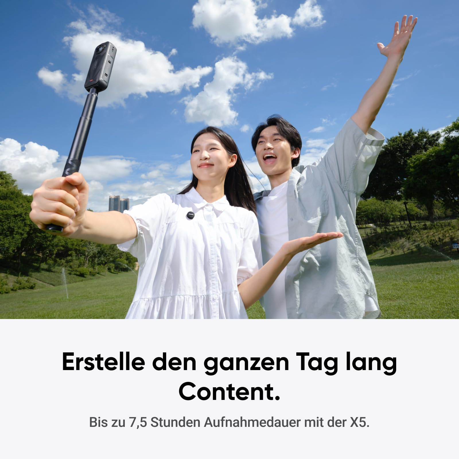 Ein Paar macht im Park ein Selfie mit einer 360-Grad-Kamera an einer Stange unter blauem Himmel mit Wolken.