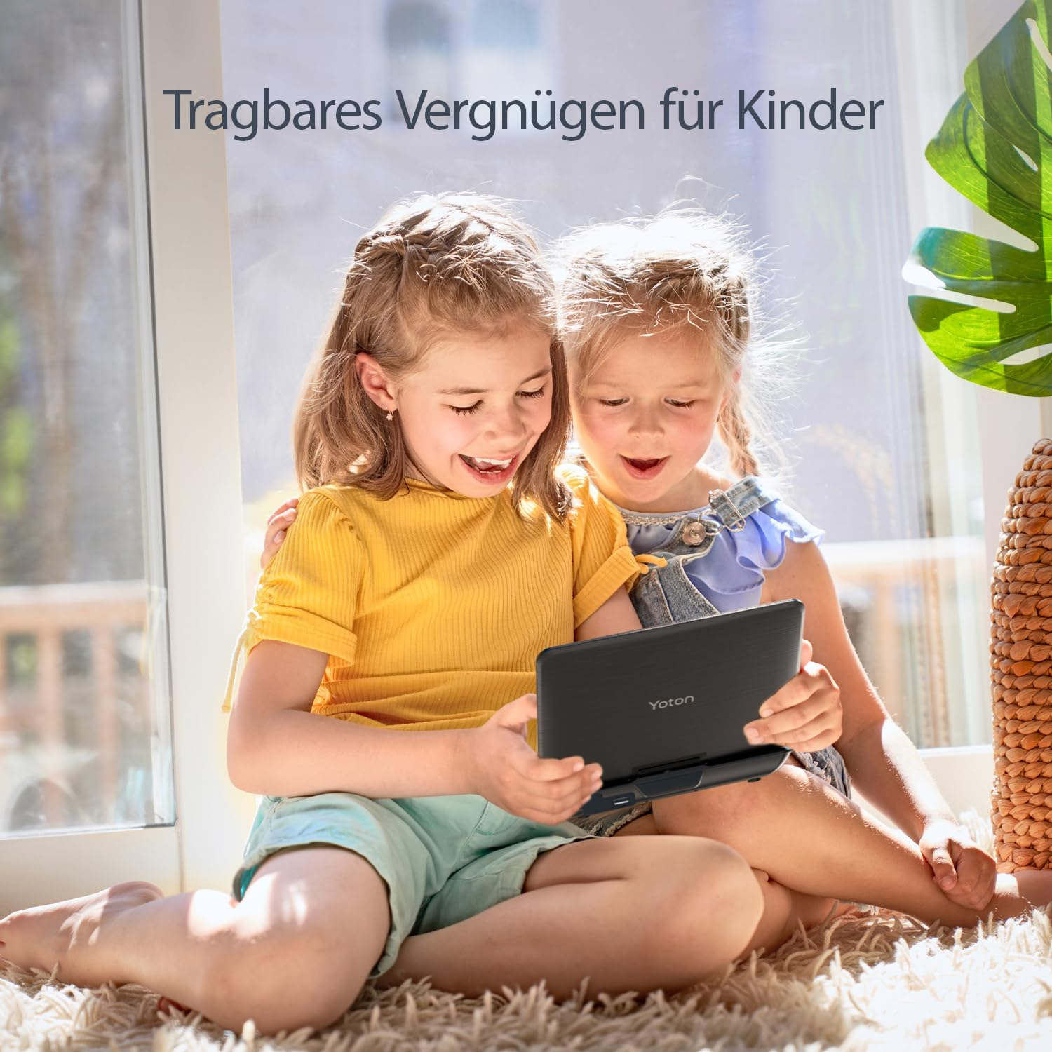 Zwei glückliche Mädchen sitzen auf einem Teppich vor einem Fenster und schauen gemeinsam in ein tragbares Yoton-Gerät.