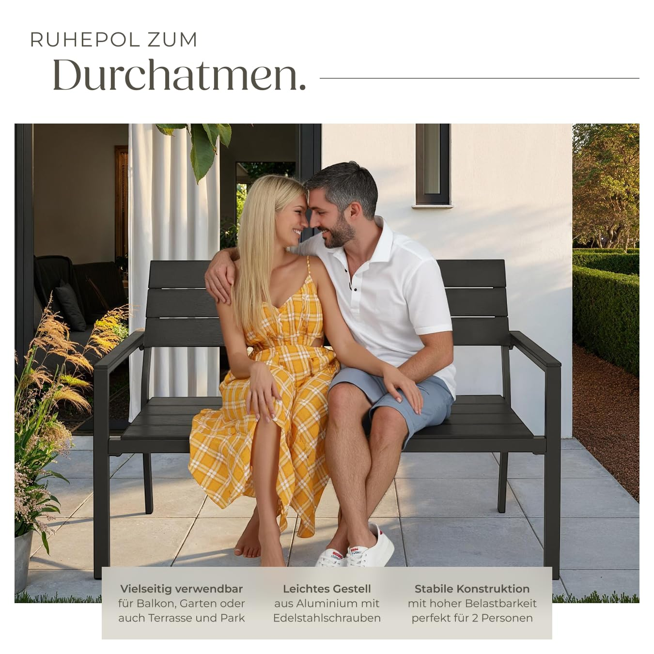Ein glückliches Paar sitzt eng umschlungen auf einer modernen schwarzen Gartenbank vor einem Haus.