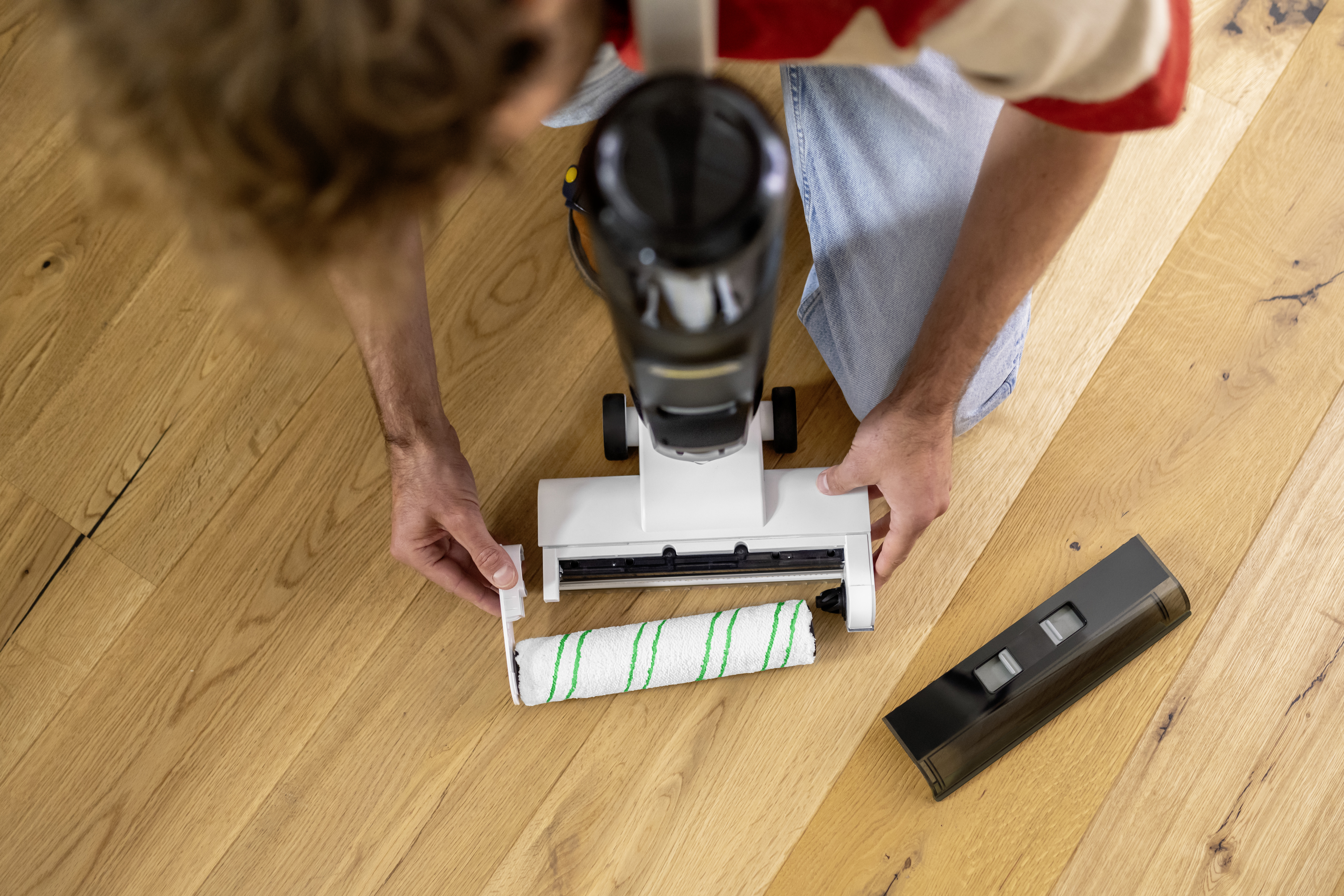 Eine Person ersetzt die Walzenbürste eines weißen und schwarzen Akkusaugers auf einem Holzboden.