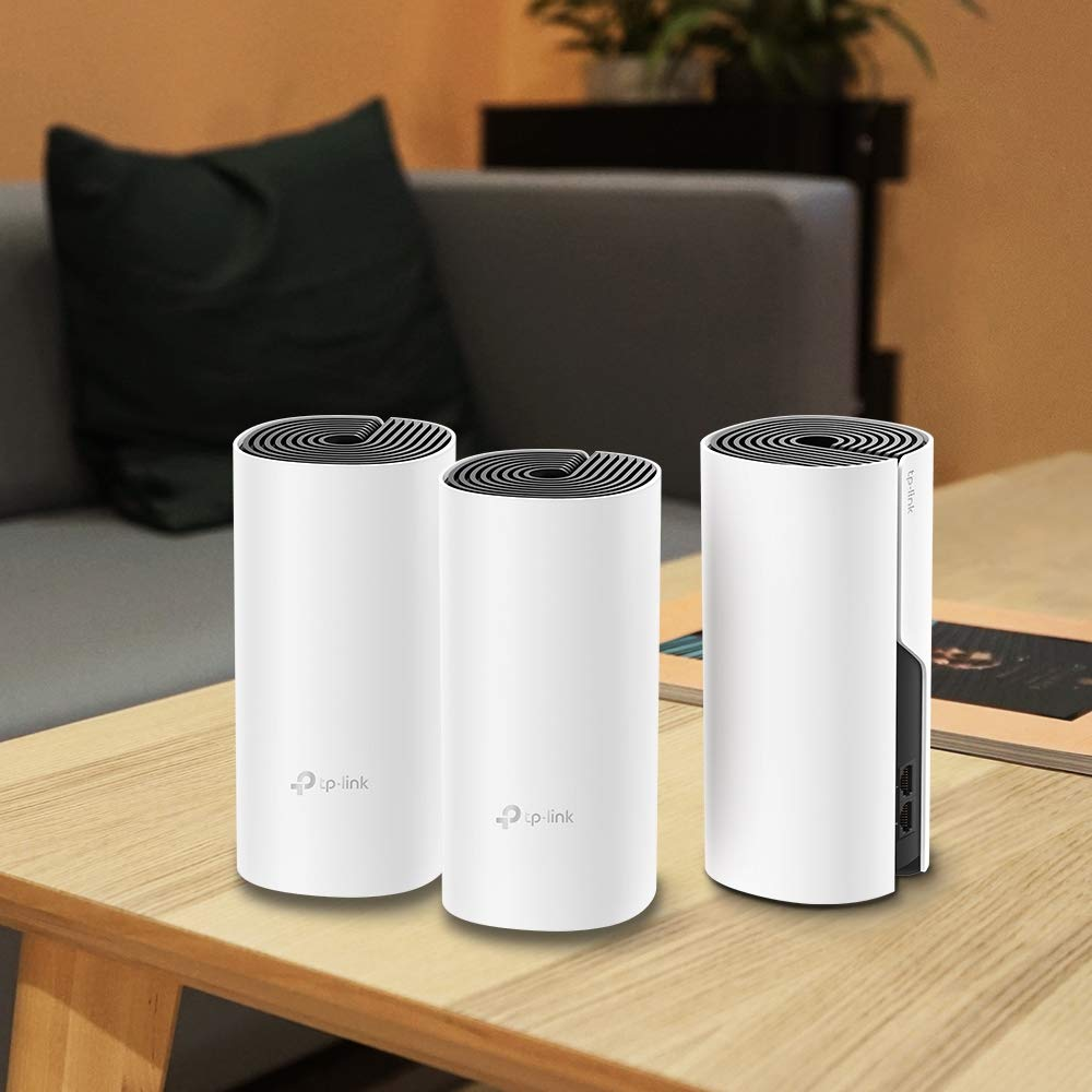 Tre router TP-Link bianchi si trovano su una scrivania di legno davanti a un divano grigio.