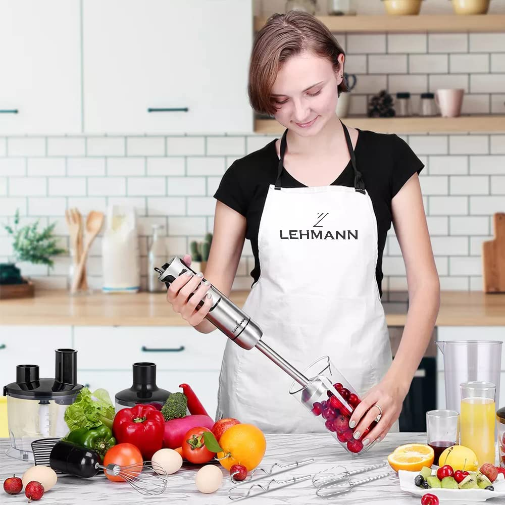 Eine Frau in einer weißen Schürze hält einen Stabmixer in einer hellen Küche mit Gemüse.