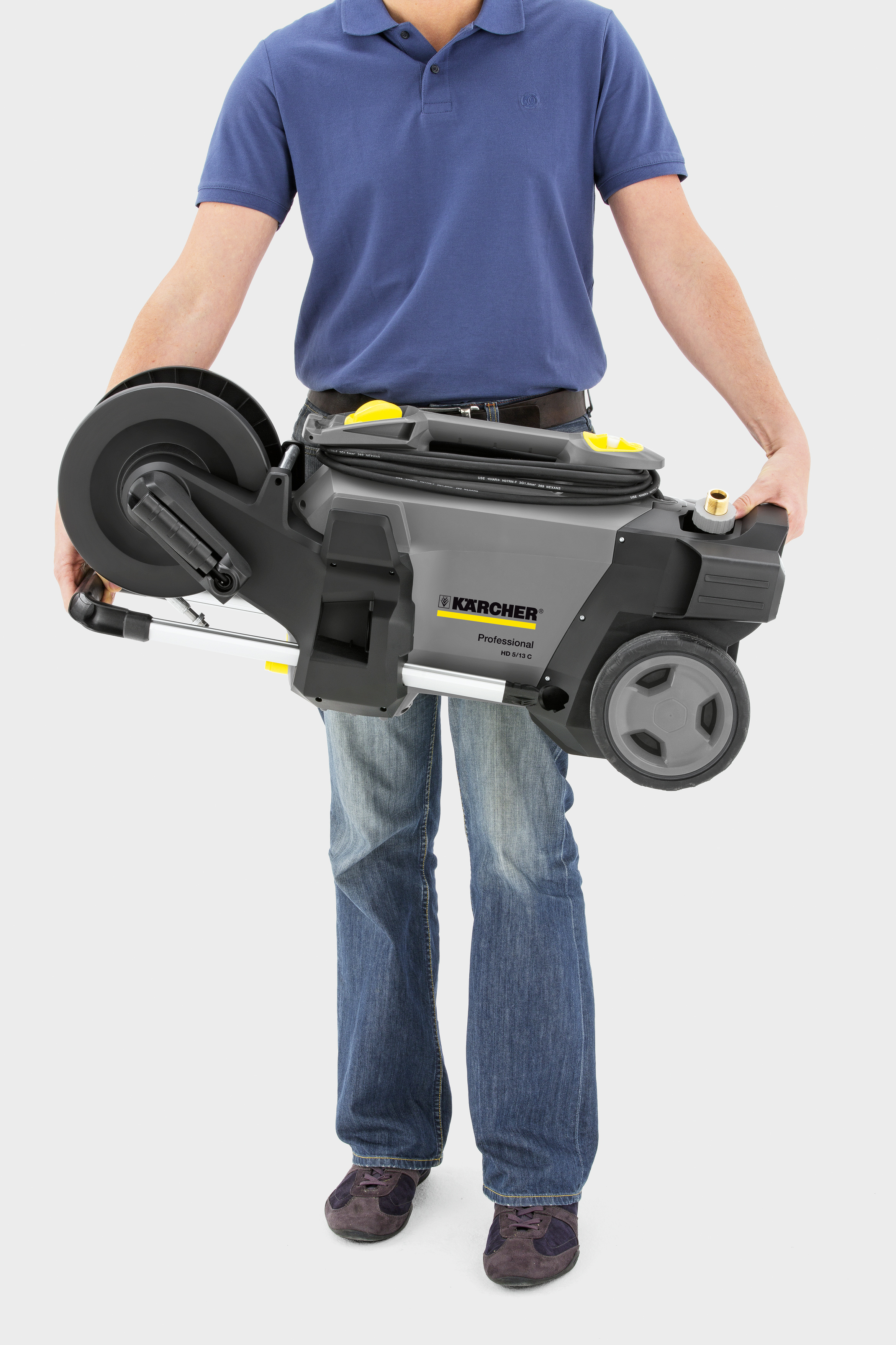 Ein Mann in blauem Poloshirt und Jeans trägt eine graue Kärcher Profi-Hochdruckreiniger.