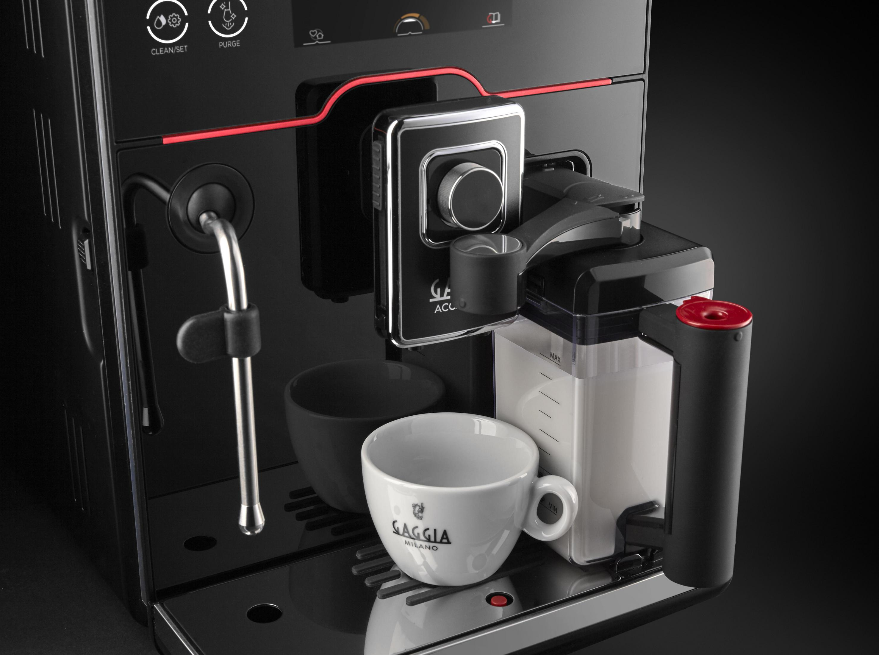 Moderne schwarze Kaffeemaschine mit weißer Tasse und Milchbehälter auf Edelstahlbasis.