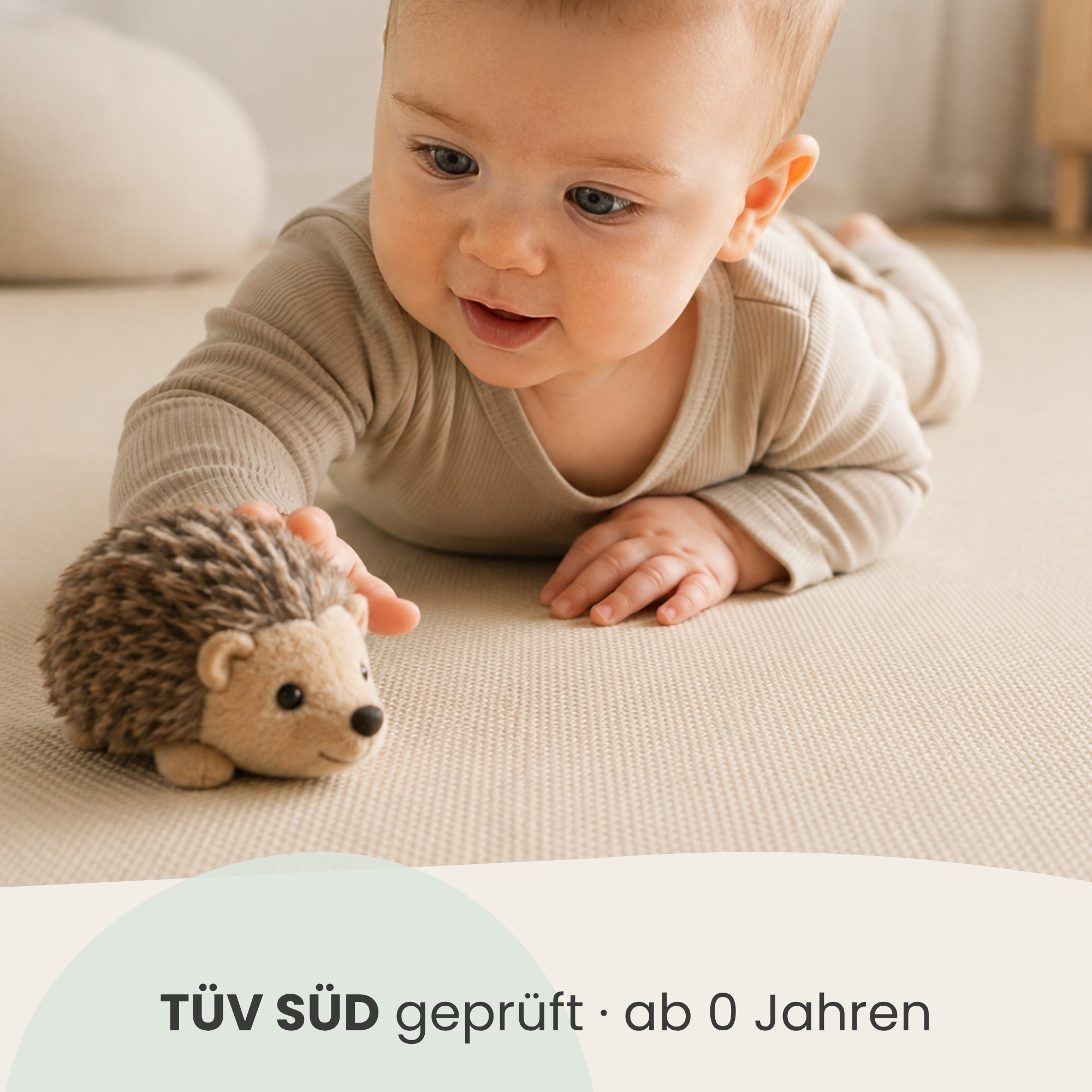 Ein Baby liegt auf einer Decke und greift nach einem Plüschigel.
