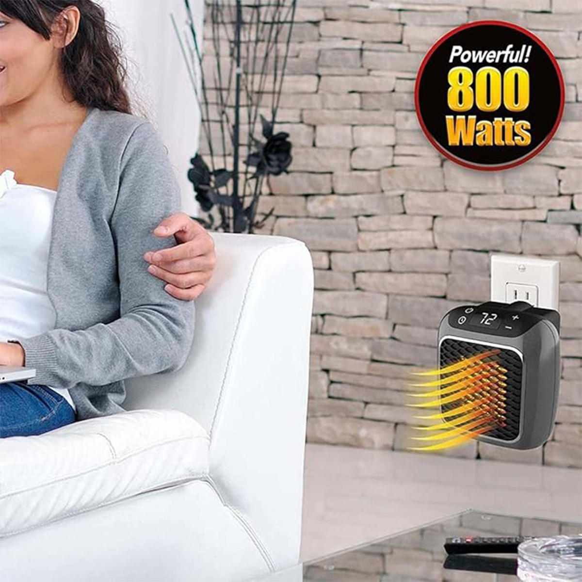 Ein kleiner 800-Watt-Heizlüfter steckt in einer Steckdose neben einer Frau auf einem weißen Sofa.