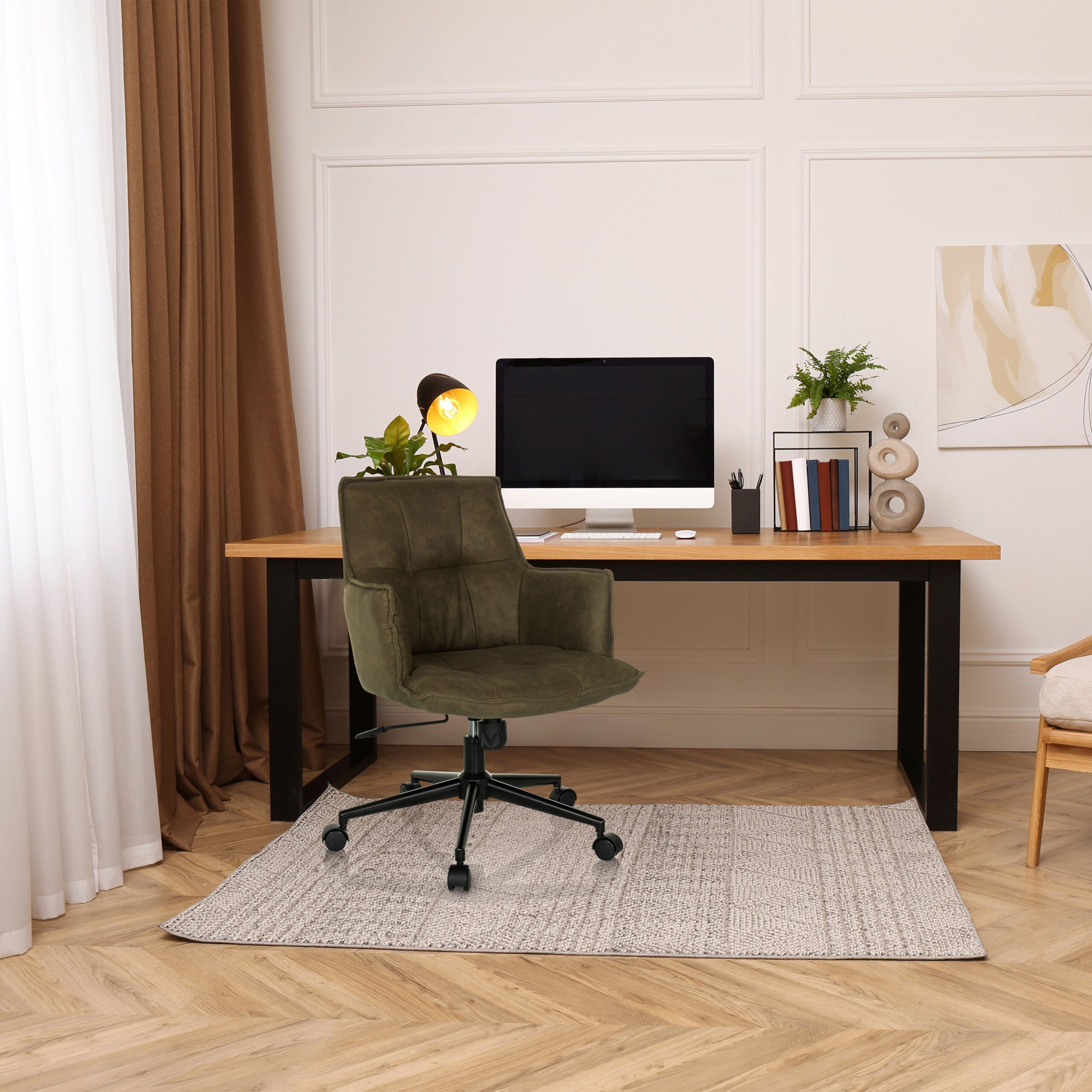 Ein moderner Schreibtisch mit Computer, grüner Drehstuhl auf einem Teppich, vor einer weißen Wand mit Kunst.