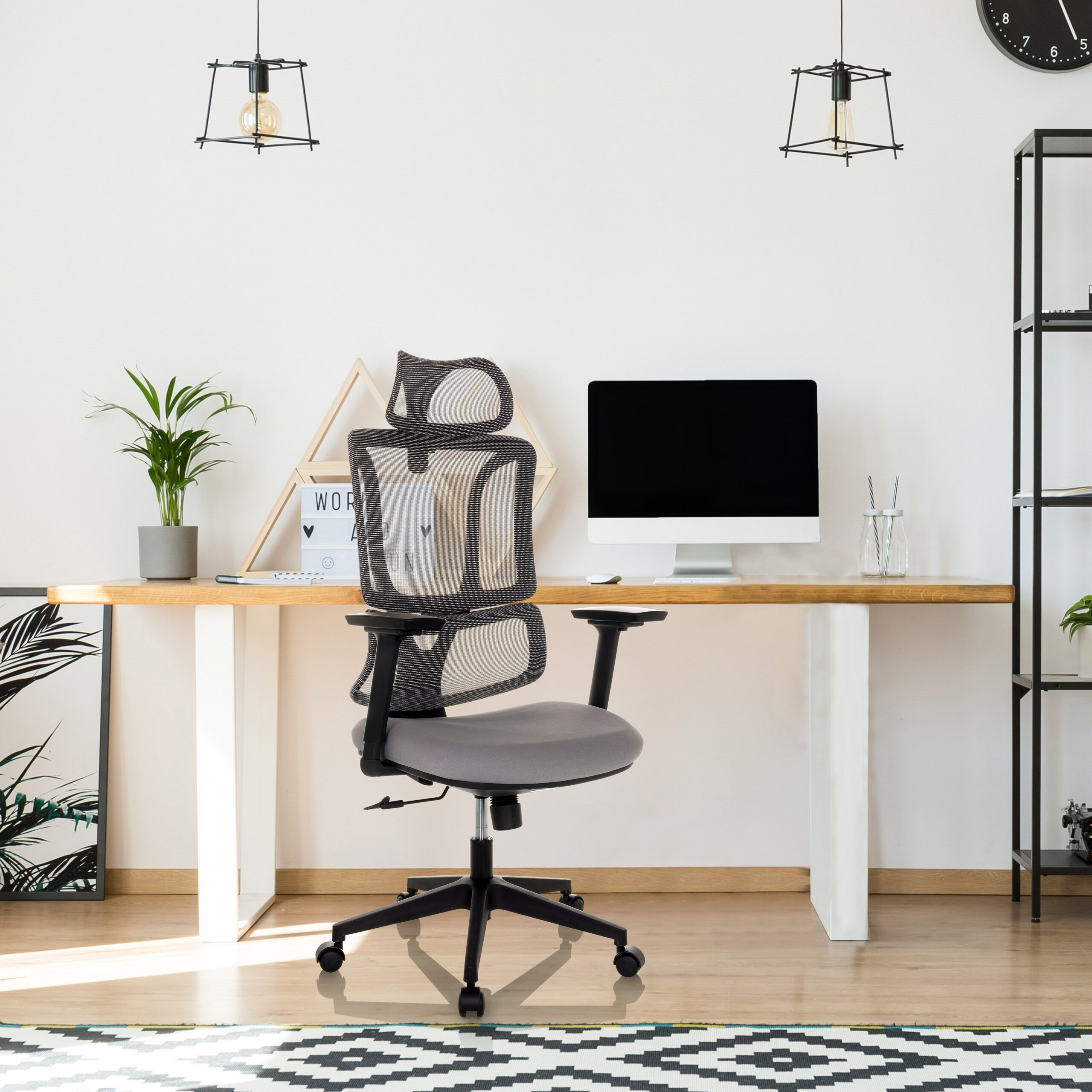 Moderne Büroeinrichtung mit grauem Schreibtischstuhl, Holztisch, Computer, Pflanzen und Leuchten an weißer Wand.