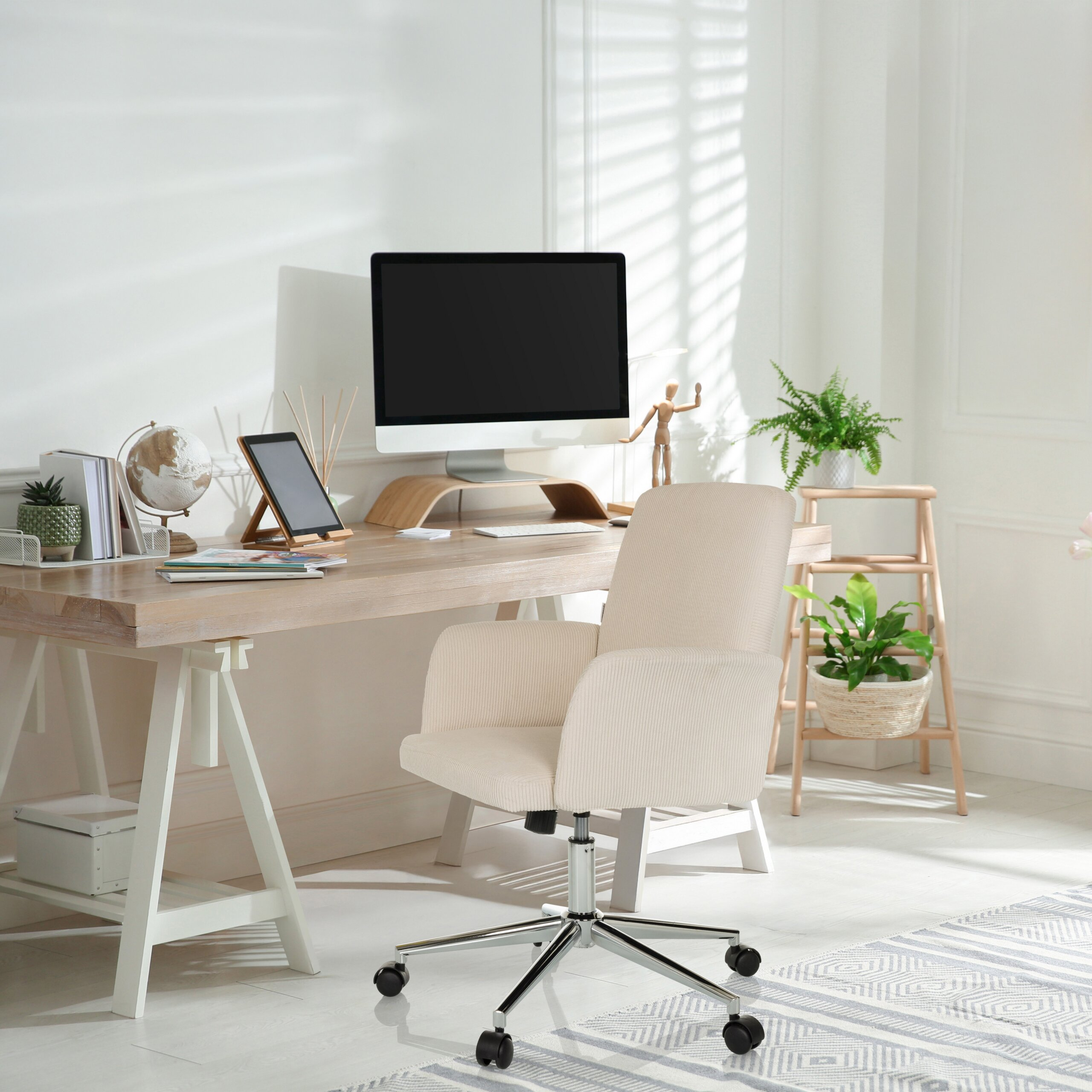 Heller Arbeitsplatz mit Holztisch, Computer, beigem Bürostuhl und grünen Pflanzen.
