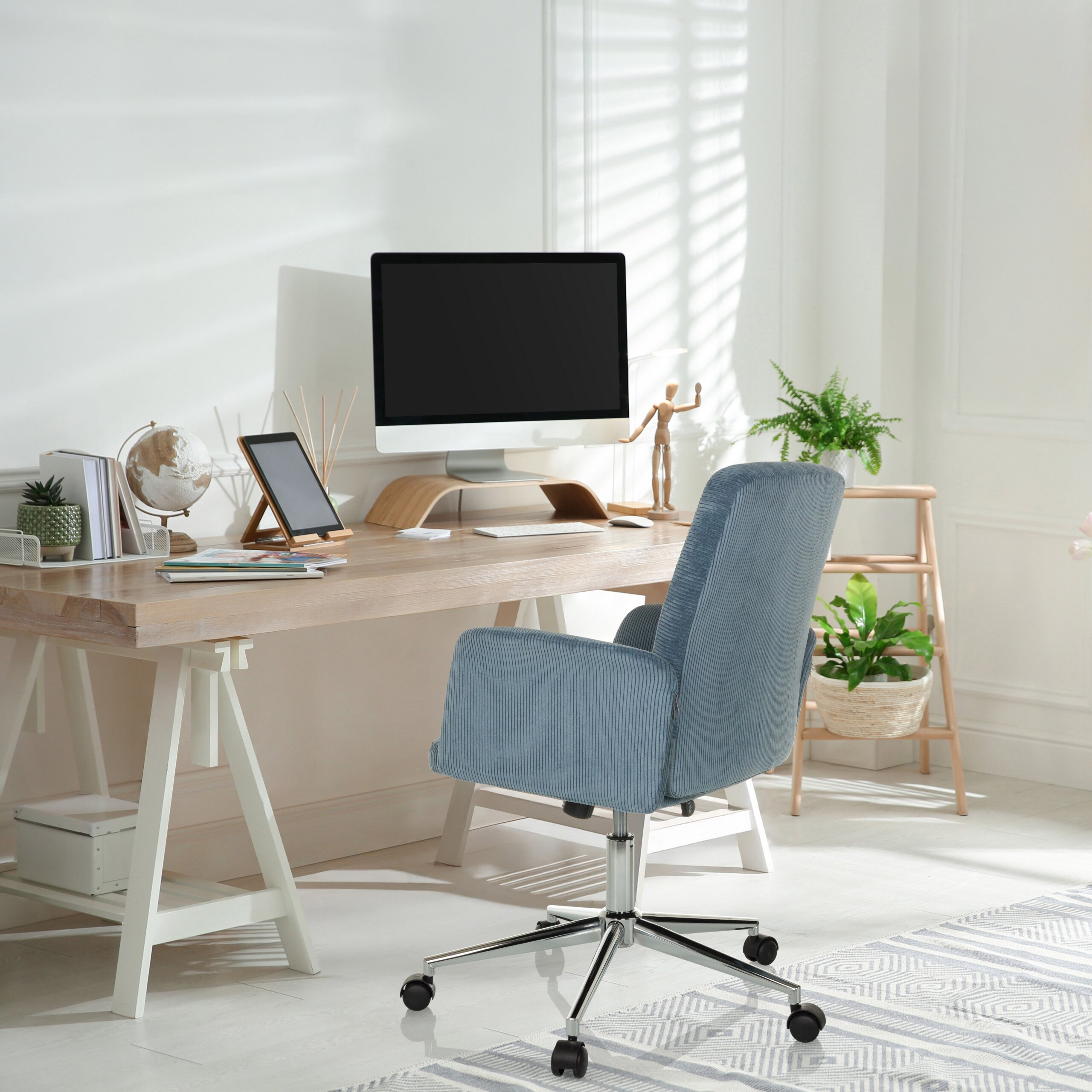 Ein ordentliches Homeoffice mit Holztisch, Computer, blauem Stuhl und Pflanzen in einem sonnigen weißen Raum.