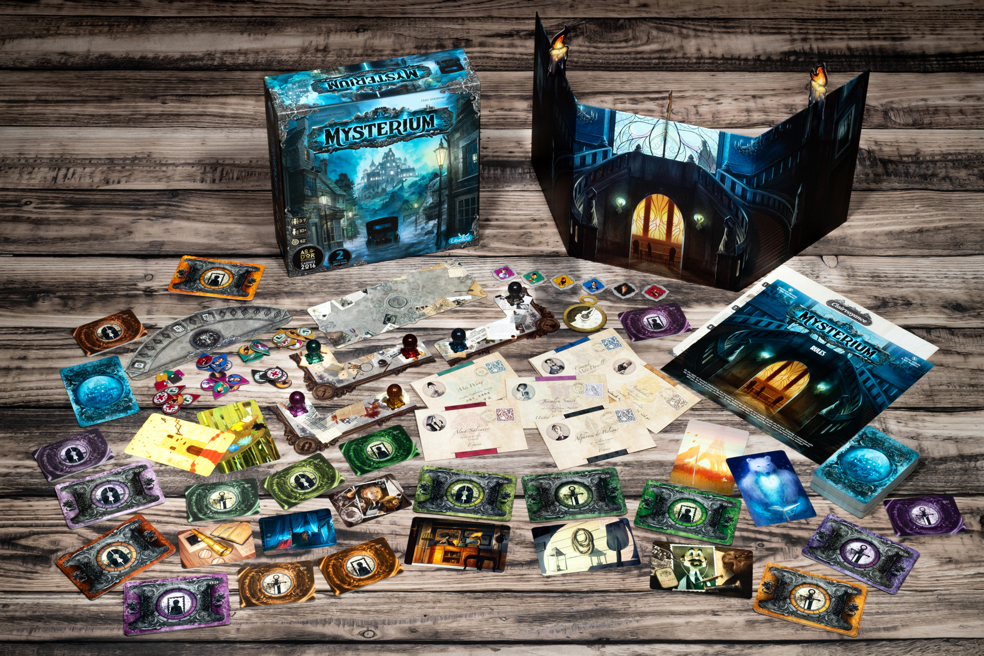 Das Brettspiel Mysterium auf einem Holztisch mit Karten, Marken, Regelbuch und Spielschachtel ausgebreitet.