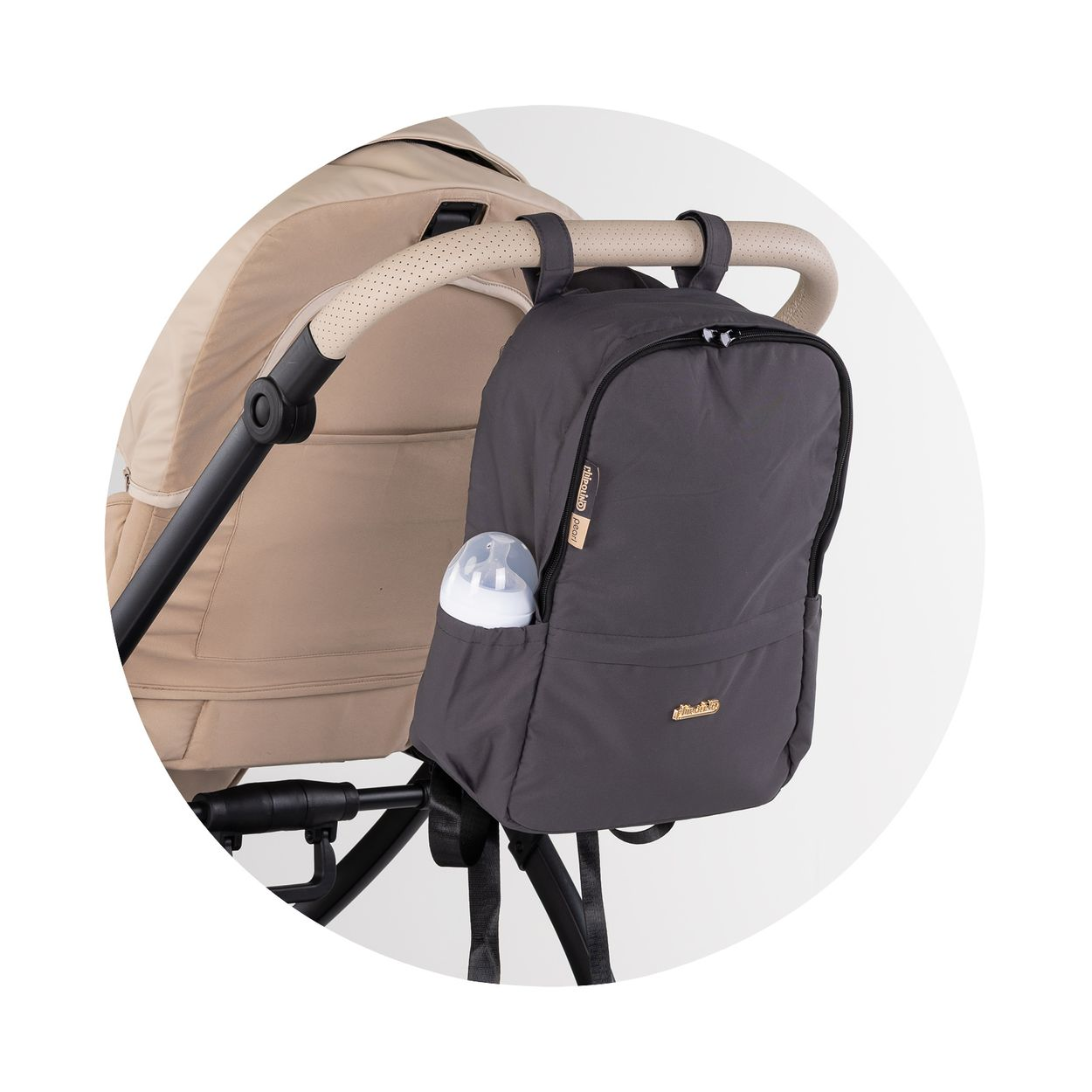 Ein grauer Rucksack mit Fläschchen in der Seitentasche hängt am Griff eines beigen Kinderwagens.