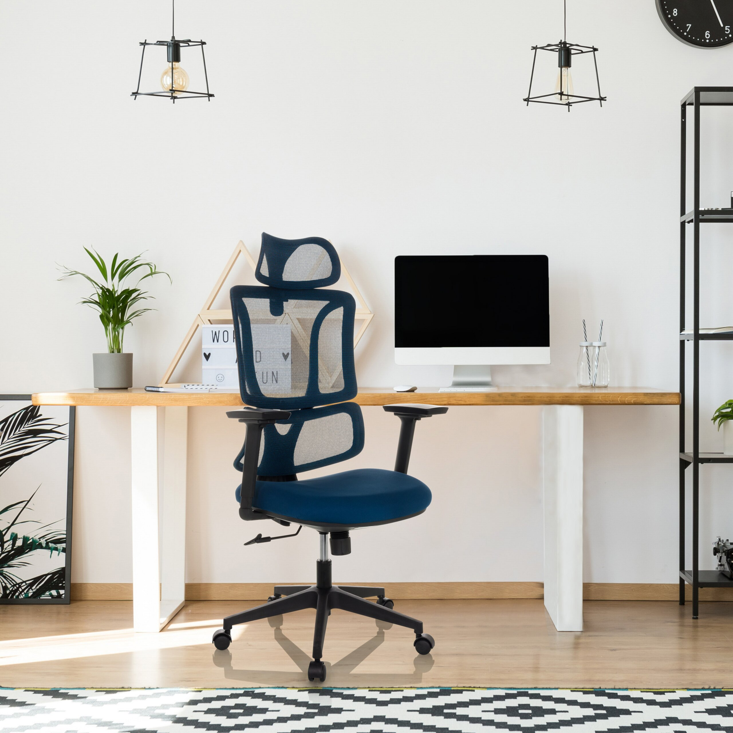 Ein moderner blauer Bürostuhl steht vor einem Holztisch mit Computer und Pflanzen.