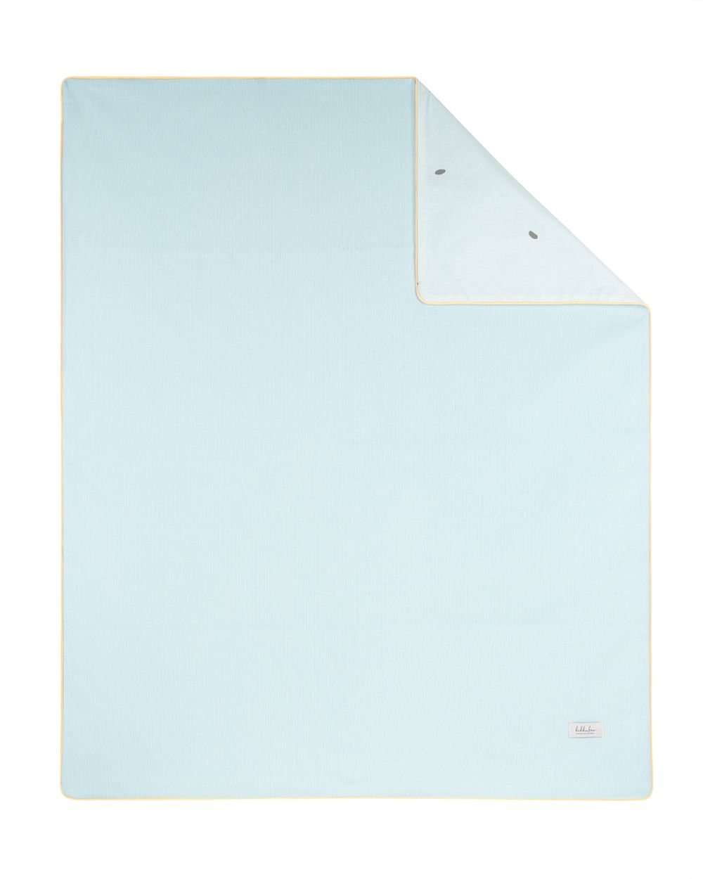 Hellblaue Bettdecke mit gelbem Rand und umgeschlagener Ecke.