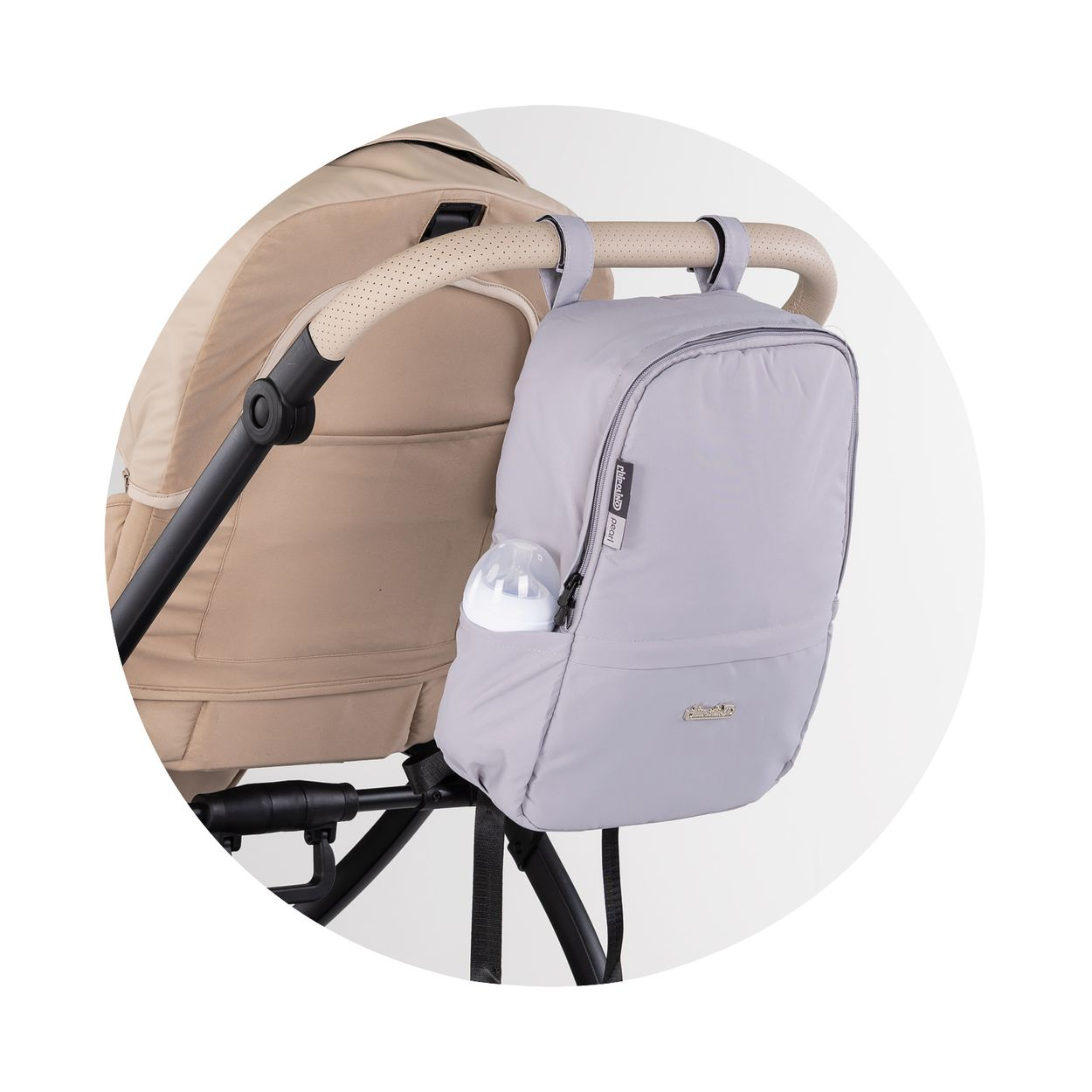 Eine hellgraue Wickeltasche hängt am Griff eines beigen Kinderwagens, mit einer Babyflasche in der Seitentasche.
