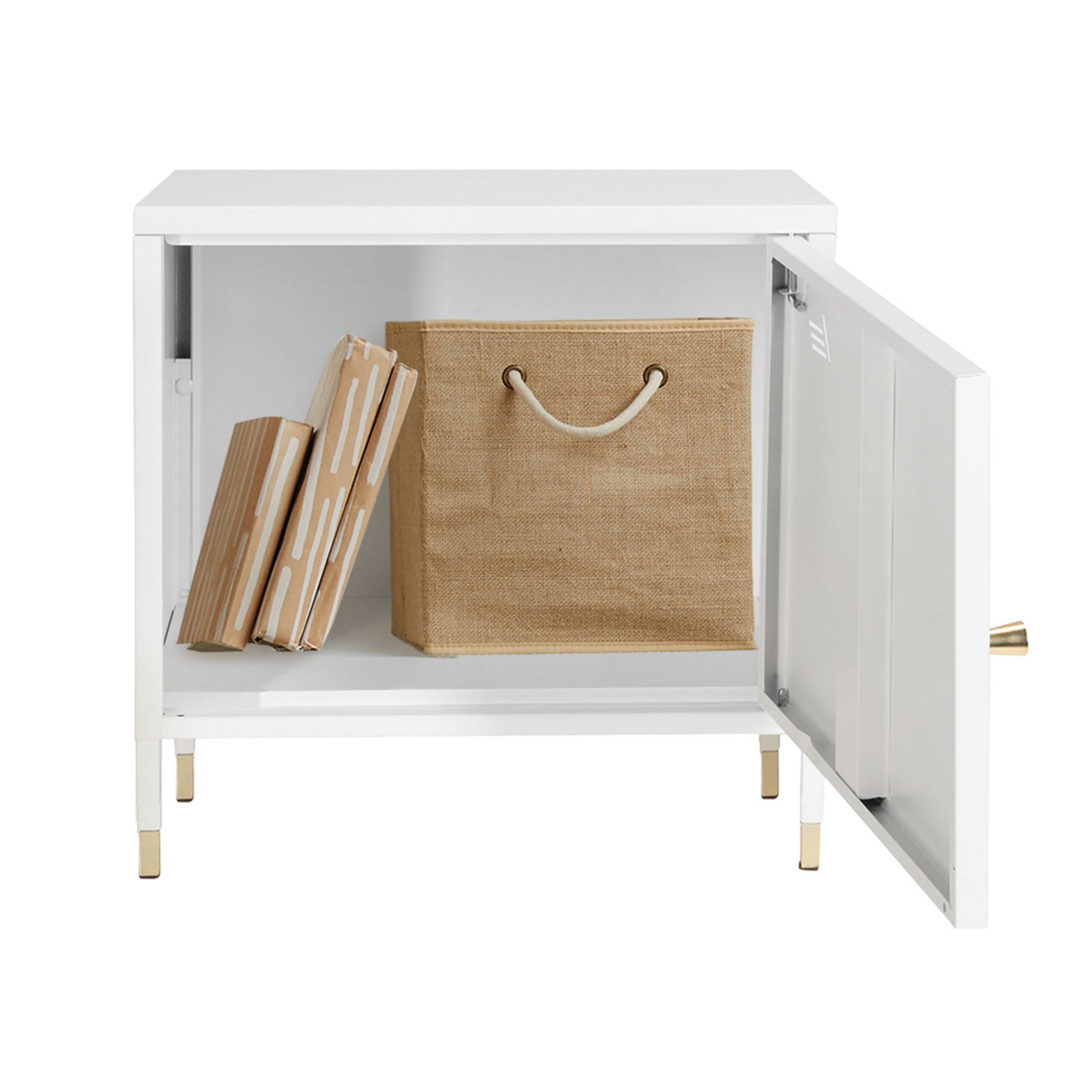 Ein weißer Schrank mit goldenen Beinen und Griff, offene Tür zeigt Bücher und eine Jute-Aufbewahrungsbox.