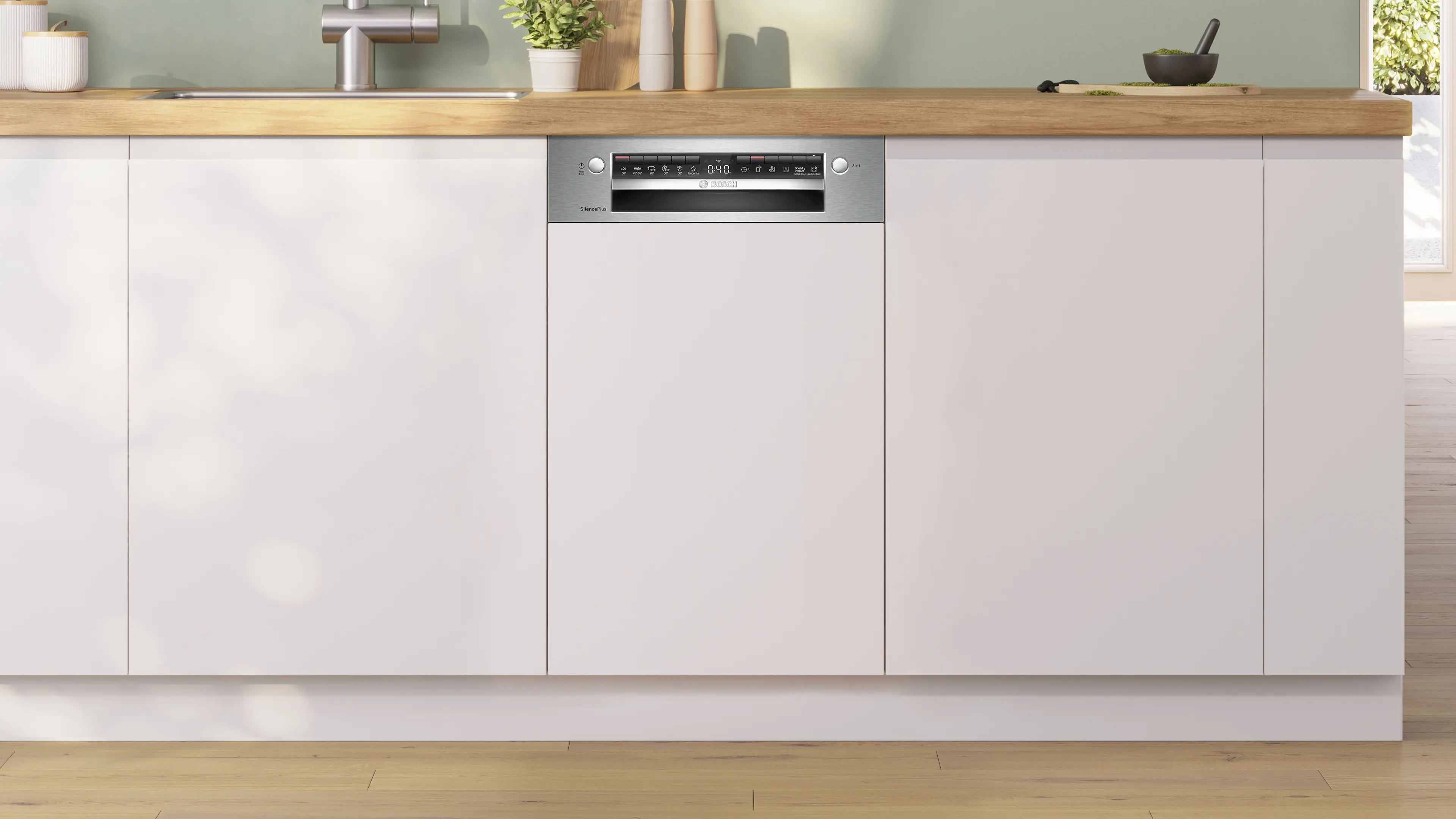Una lavastoviglie bianca da incasso con pannello in acciaio inox sotto un piano di lavoro in legno in una cucina luminosa.