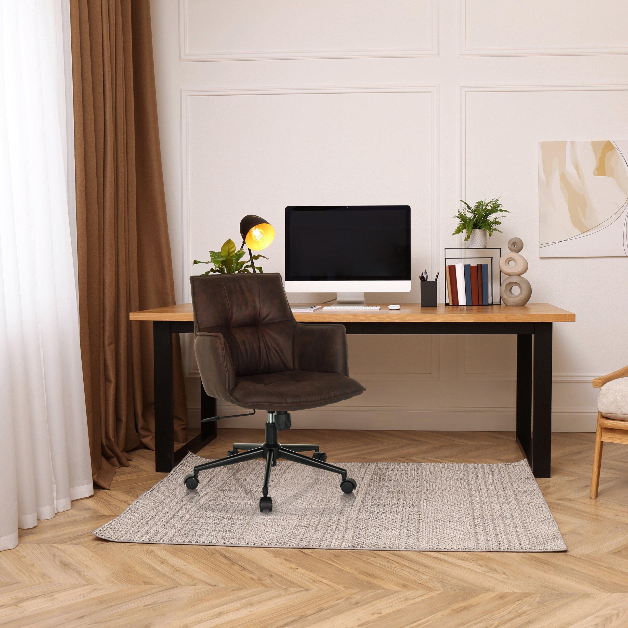 Moderne Arbeitsplatz mit einem braunen Ledersessel, Holztisch, Computer und Wandkunst in einem hellen Raum.