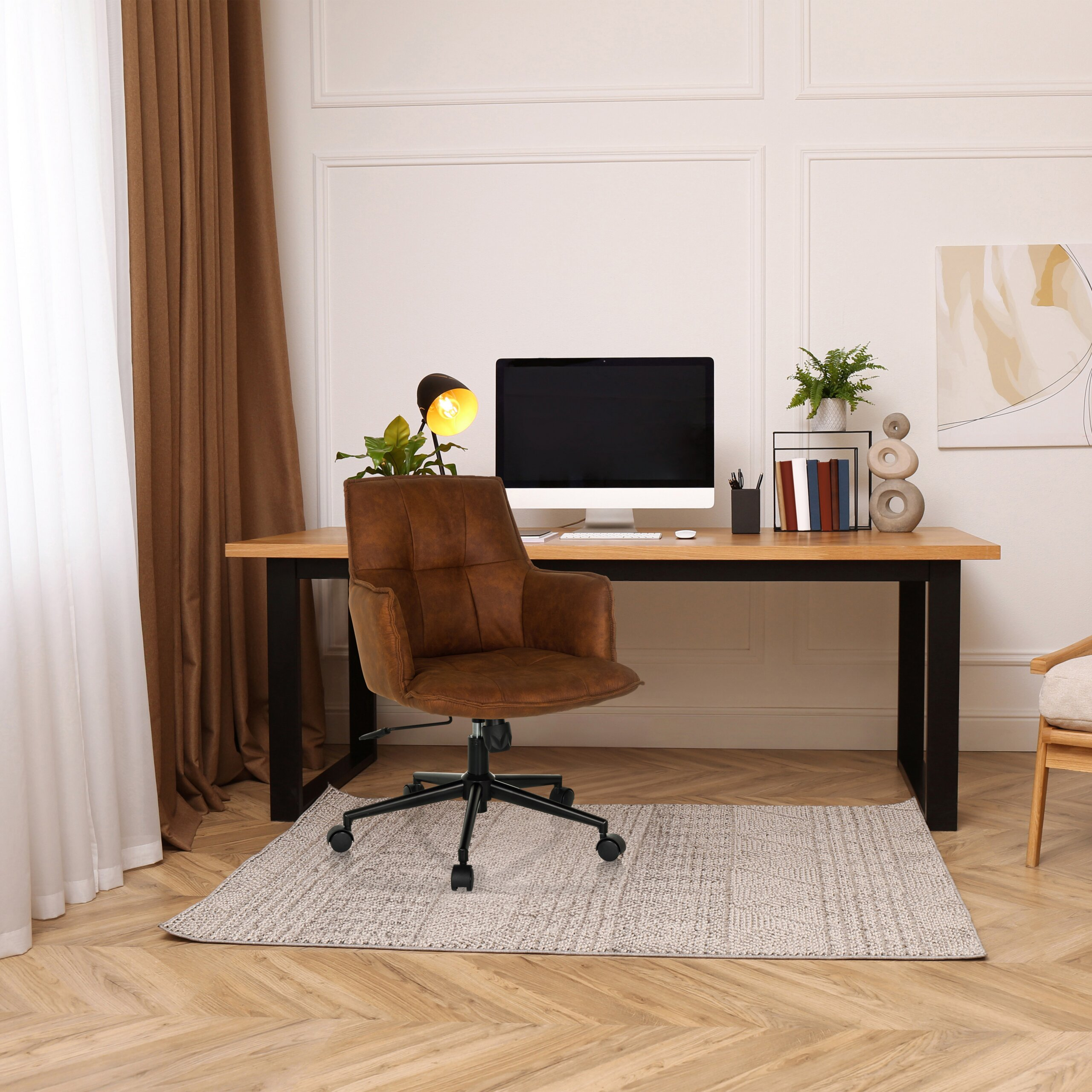 Moderne Büroecke mit braunem Ledersessel, Holztisch, Computer und Wandbild vor weißer Wand.