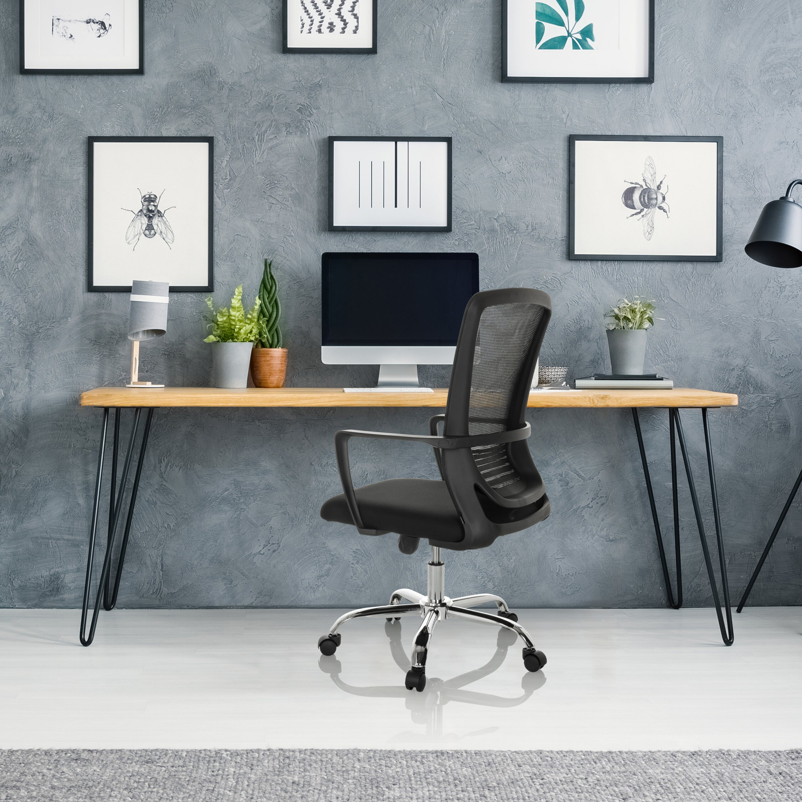 Moderne Schreibtisch mit Computer, Stuhl und Bildern an der grauen Wand.
