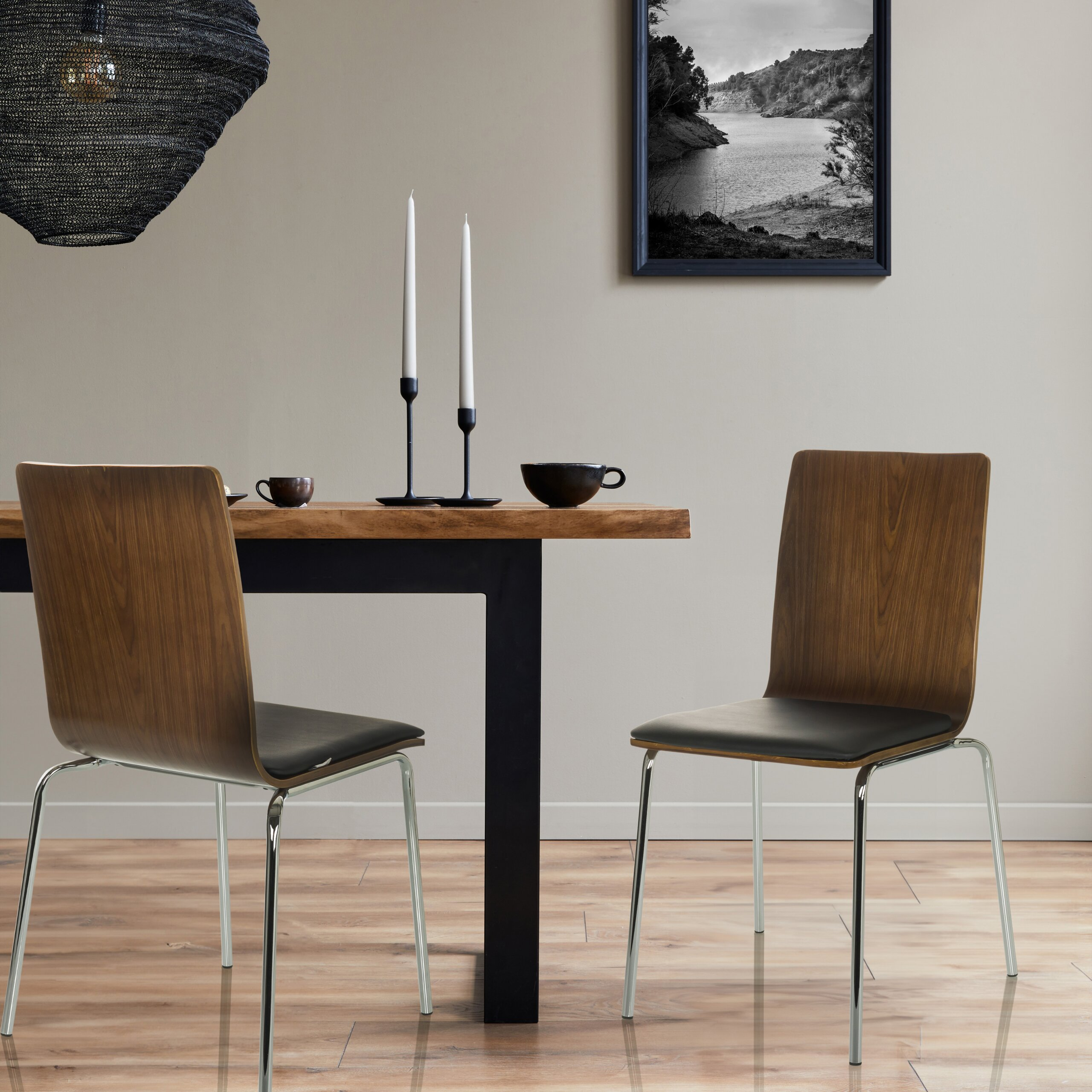 Ein hölzernes Esszimmer-Set mit zwei Stühlen, Kerzenhaltern, einer Tasse und einem gerahmten Landschaftsbild an der Wand.