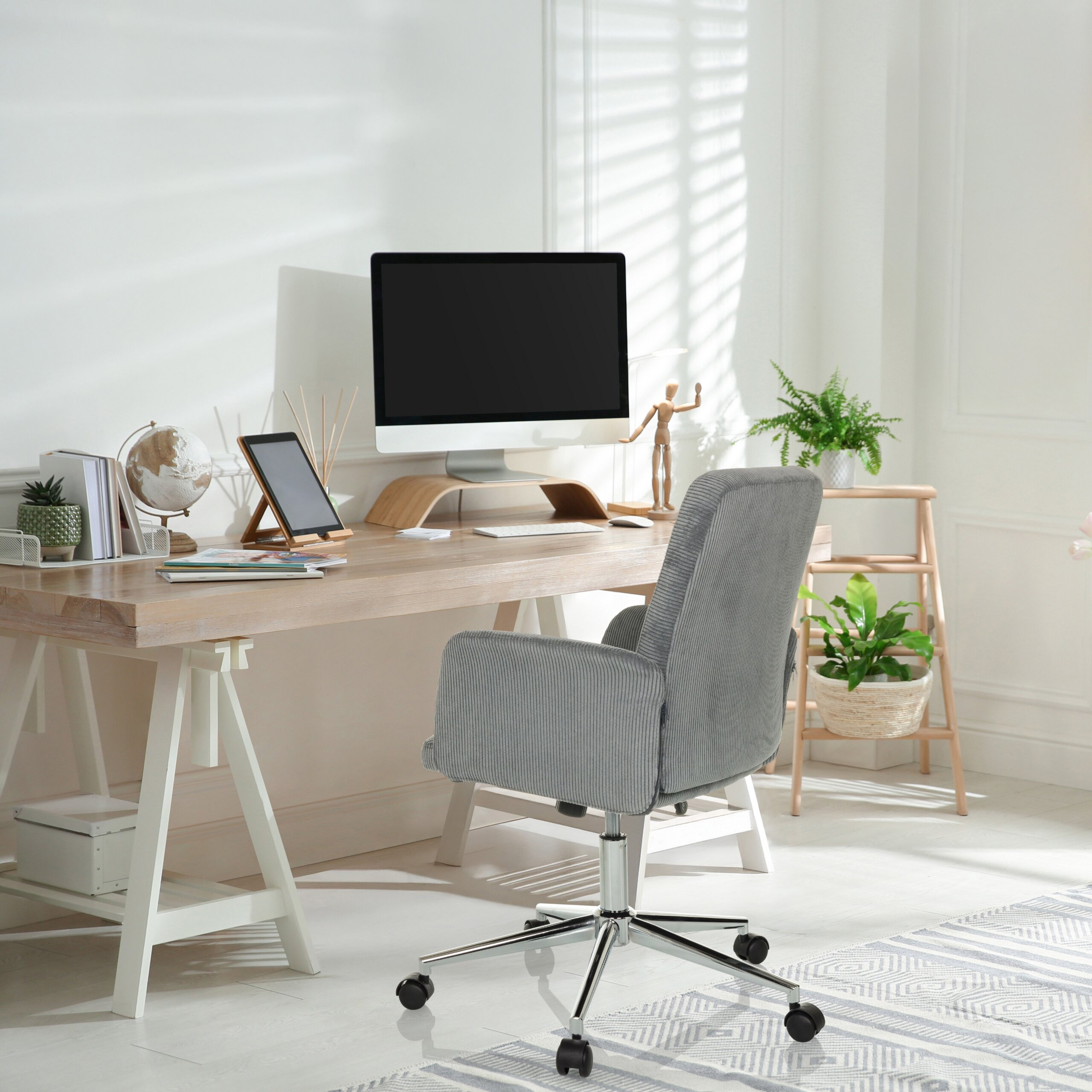 Ein heller Arbeitsplatz mit Computer, Holztisch, grauem Bürostuhl und Zimmerpflanzen am Fenster.